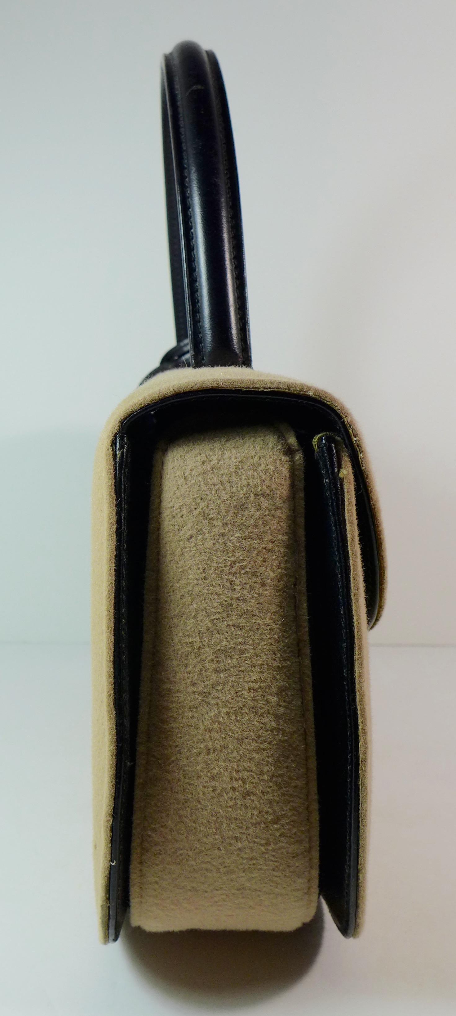 This Gucci tan wool purse features a black bar closure, black leather handle, and attached leather logo tag. 

Small scattered moth holes in the wool.
See photographs please.

Measurements in Inches: 
Height: 7
Width: 11
Length: 3
Handle: 12 