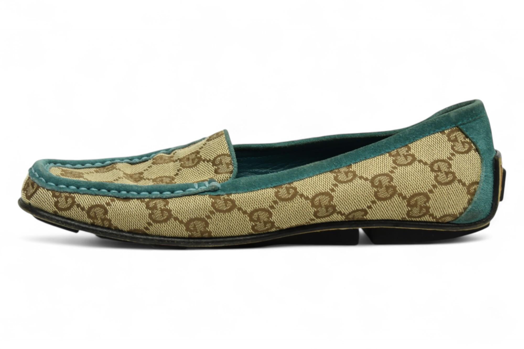 Classic meets comfort in these Gucci monogram loafers, crafted from beige GG canvas and accented with rich teal suede trim. Designed for effortless style, they feature a sleek moc-toe silhouette and durable rubber-inset soles for grip and ease of