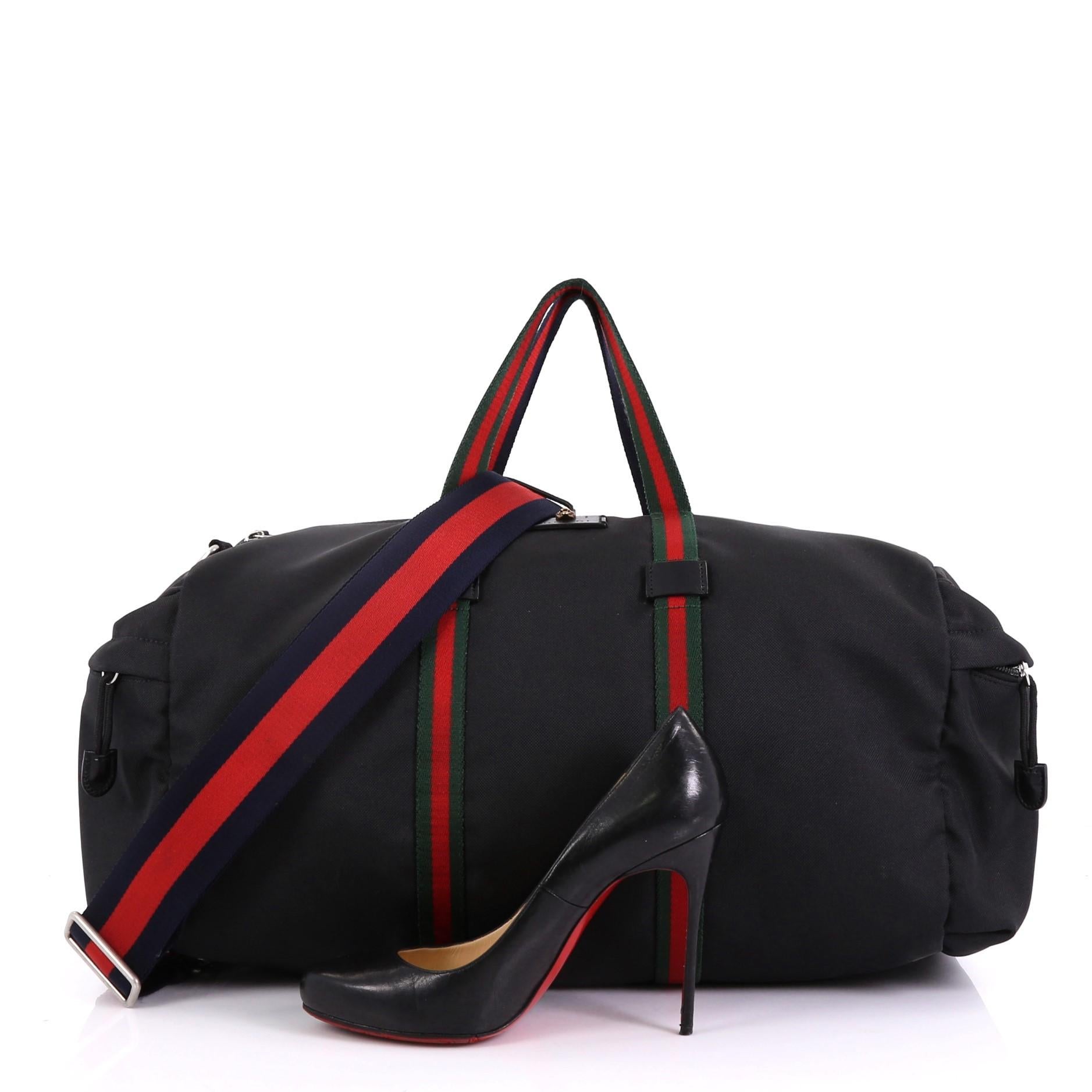 This Gucci Technical Duffle Bag Techno Canvas Large, crafted in black canvas, features green and red canvas top handles with blue and red on the opposite side, black leather trim, and aged silver-tone hardware. Its zip closure opens to a black nylon