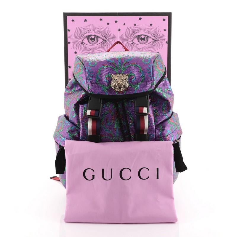 This Gucci Techpack Backpack Brocade, crafted from purple and multicolor brocade, features web shoulder straps, adjustable front web straps with buckles, exterior zip pockets, metal feline detail, and aged gold-tone hardware. Its drawstring closure