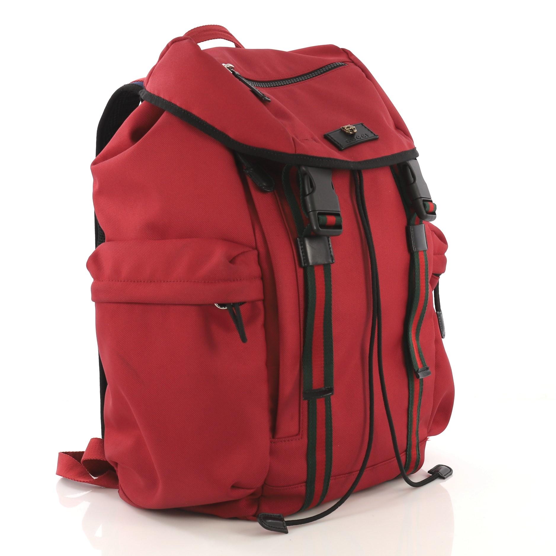 This Gucci Techpack Backpack Techno Canvas, crafted from red canvas, features Web shoulder straps, Web adjustable front straps with plastic buckles, exterior zip pockets, Gucci tag with metal feline detail, and silver-tone hardware. Its drawstring