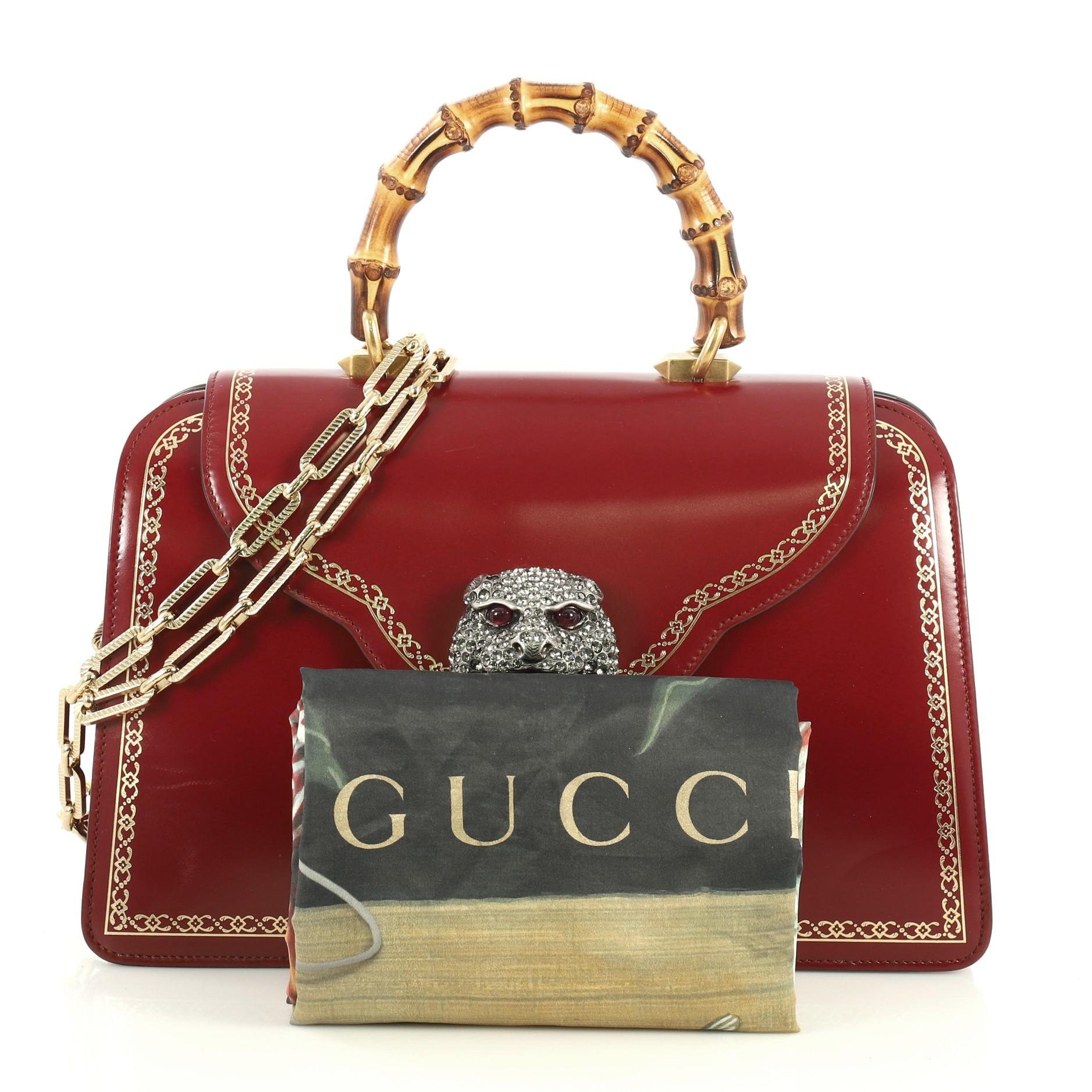 This Gucci Thiara Top Handle Bag Frame Print Leather Medium, crafted from red leather, features bamboo top handle, crystal-embellished tiger head on its flap, and aged gold-tone hardware. Its magnetic snap closure opens to a printed satin interior