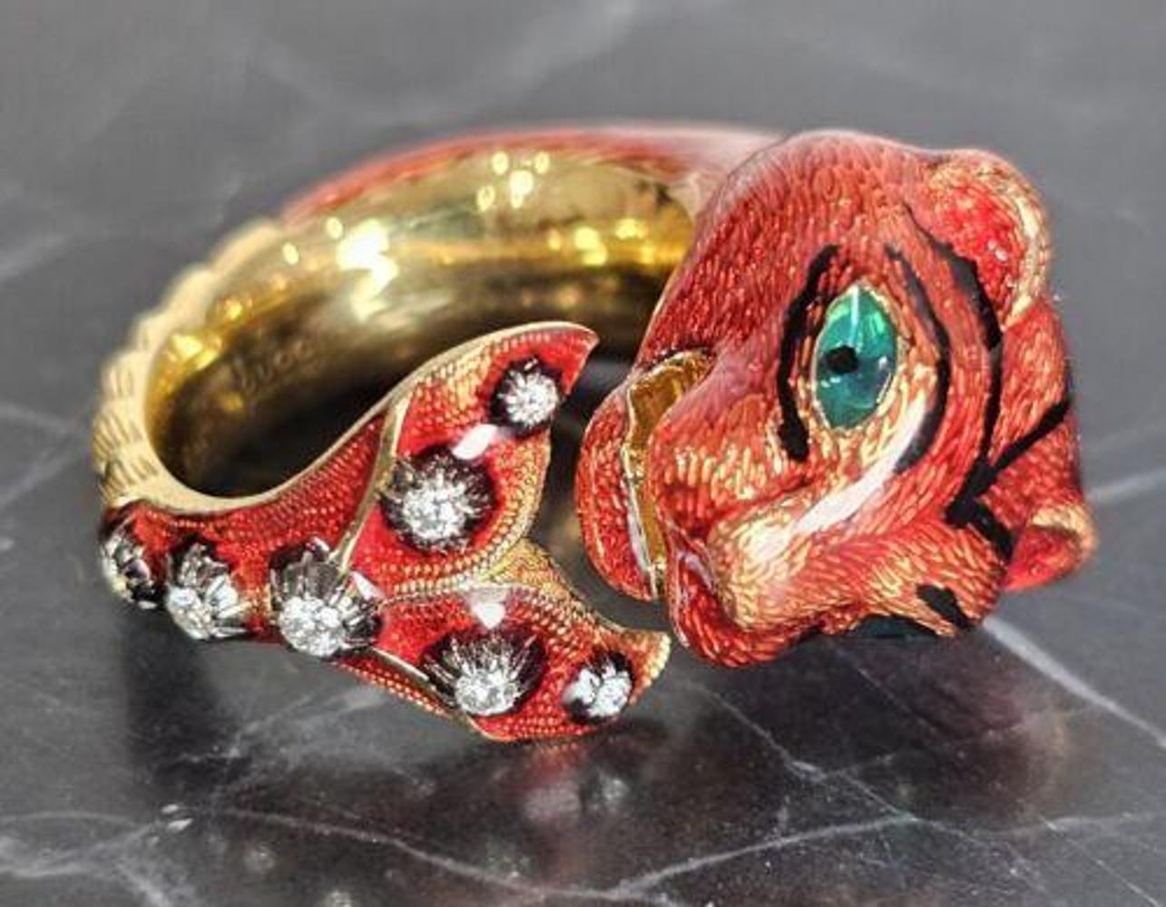 The Gucci Tiger Ring is a luxurious piece of fine jewelry crafted from 18k yellow gold, featuring striking red enamel detailing on the tiger design. The ring is adorned with sparkling diamonds as the main stone, adding a touch of elegance and