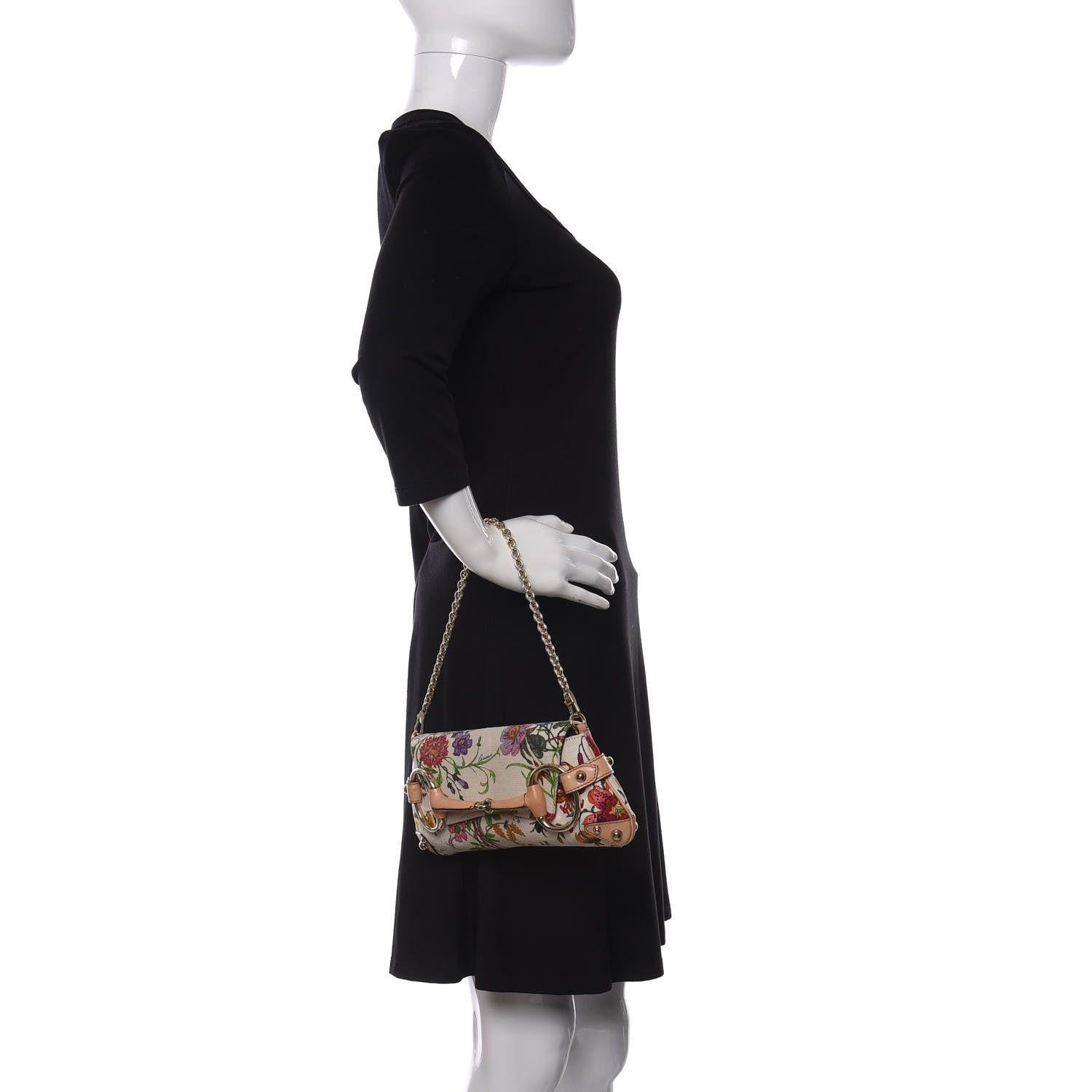 This clutch is made of bright and colourful floral print canvas. The clutch features a polished brass chain link wrist strap, beige leather trim and a large frontal polished brass horsebit detail wrapped in leather. The frontal flap opens to a