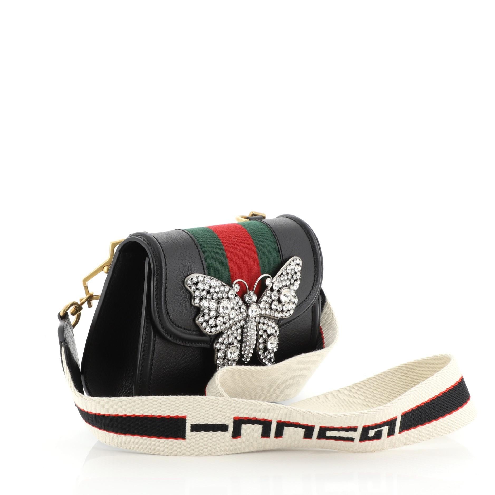 This Gucci Totem Shoulder Bag Leather Small, crafted in black leather, features a detachable Gucci jacquard stripe shoulder strap, front flap with enameled metal butterfly ornament, web detailing and gold and silver-tone hardware. Its magnetic