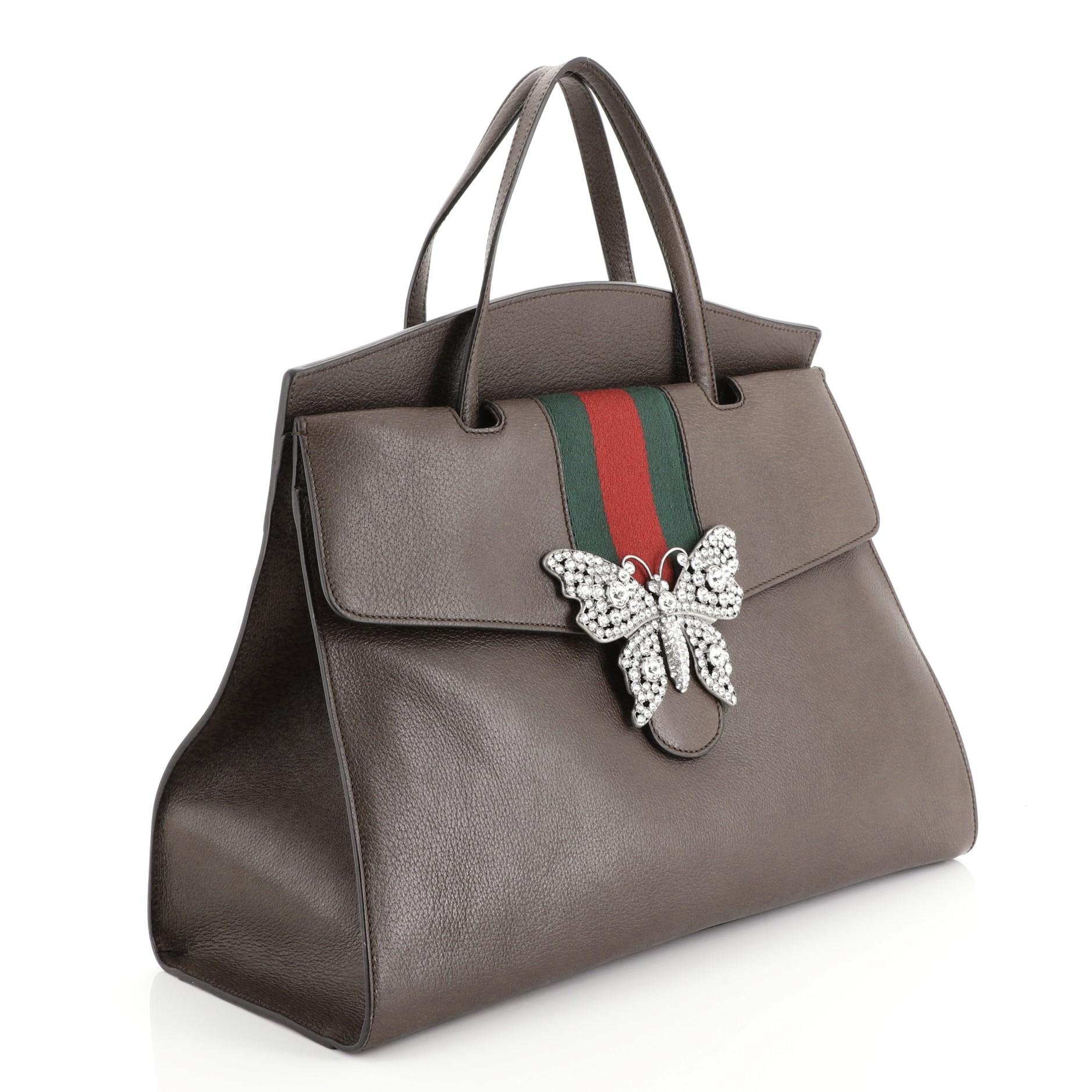 This Gucci Totem Top Handle Bag Leather Large, crafted from brown leather, features dual leather top handles, green and red web with crystal butterfly ornament, and silver-tone hardware. Its press-lock closure opens to a neutral microfiber interior