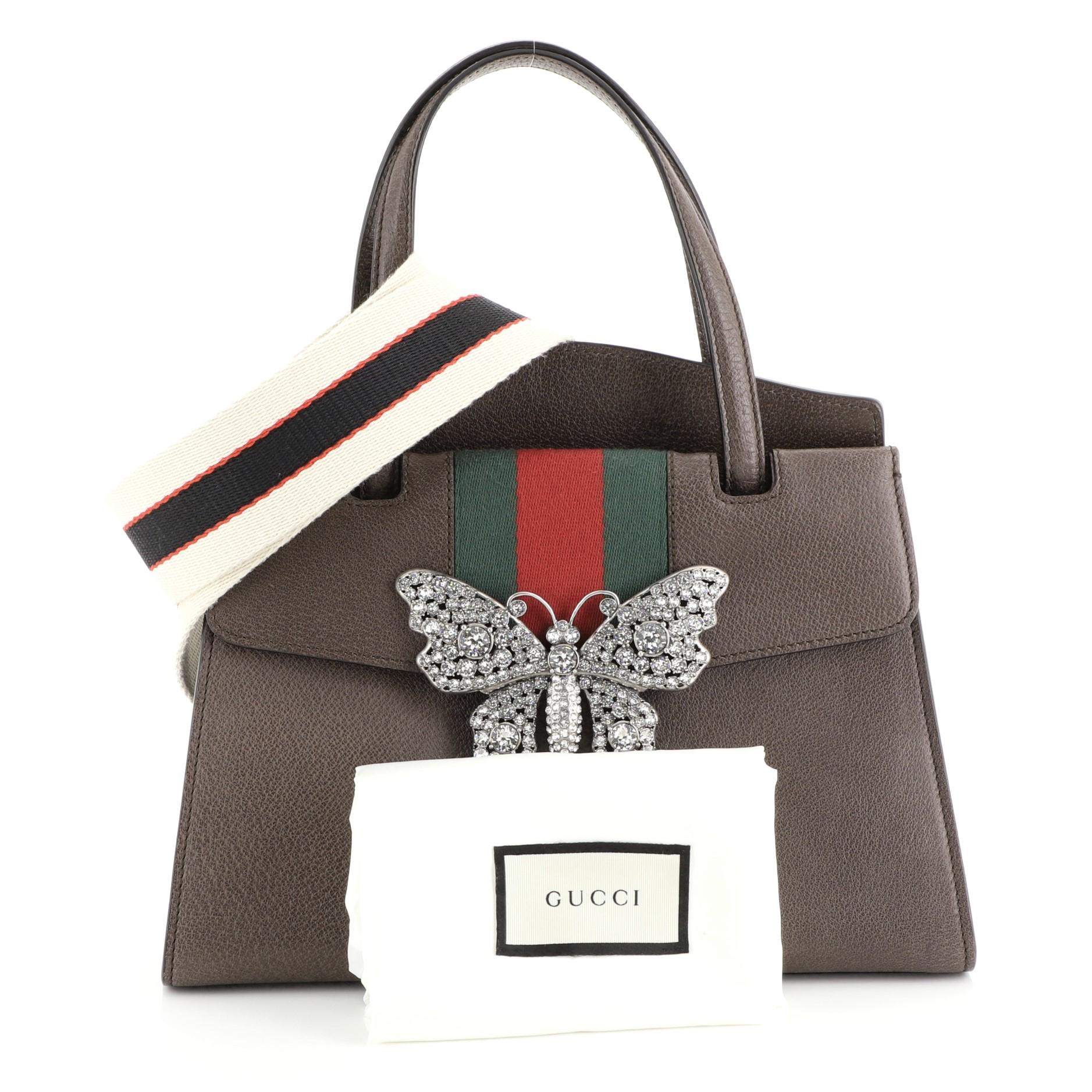 This Gucci Totem Top Handle Bag Leather Medium, crafted from brown leather, features dual leather top handles, green and red web stripe with crystal butterfly ornament, and aged gold-tone hardware. Its press-lock closure opens to a neutral
