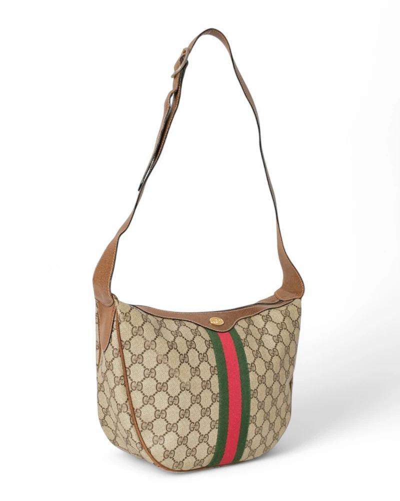 Sac Gucci signature, modèle Hobo, en toile GG Supreme avec inserts marron et ferrures dorées. Doté d'une fermeture à glissière sur le dessus et d'un intérieur doublé de daim avec une poche pratique, le sac est assez spacieux. Équipé d'une