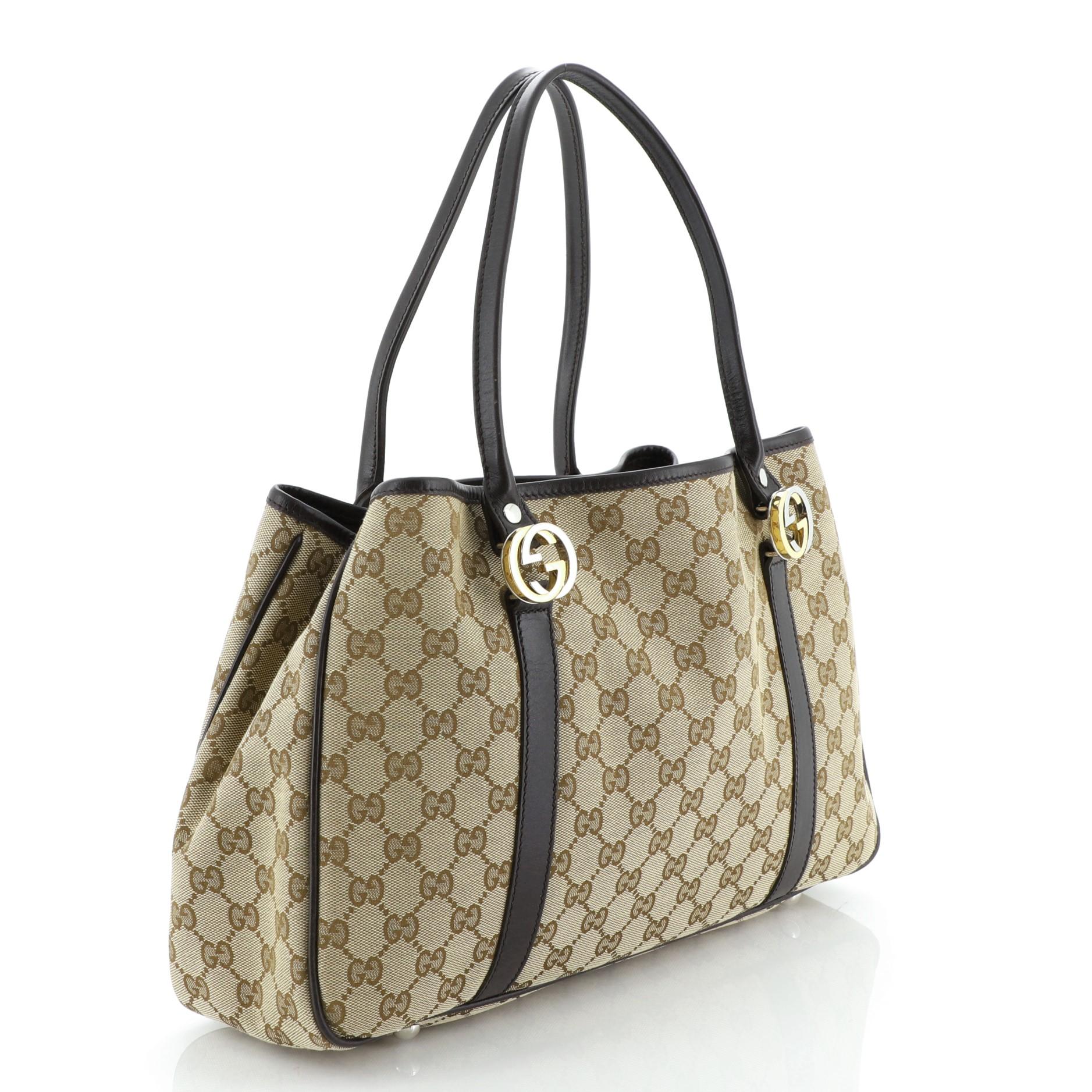 This Gucci Twins Tote GG Canvas Medium, crafted from brown GG canvas, features dual tall handles with interlocking GG logo hardware, leather trim, and gold and silver-tone hardware. It opens to a brown fabric interior with side zip and slip pockets.