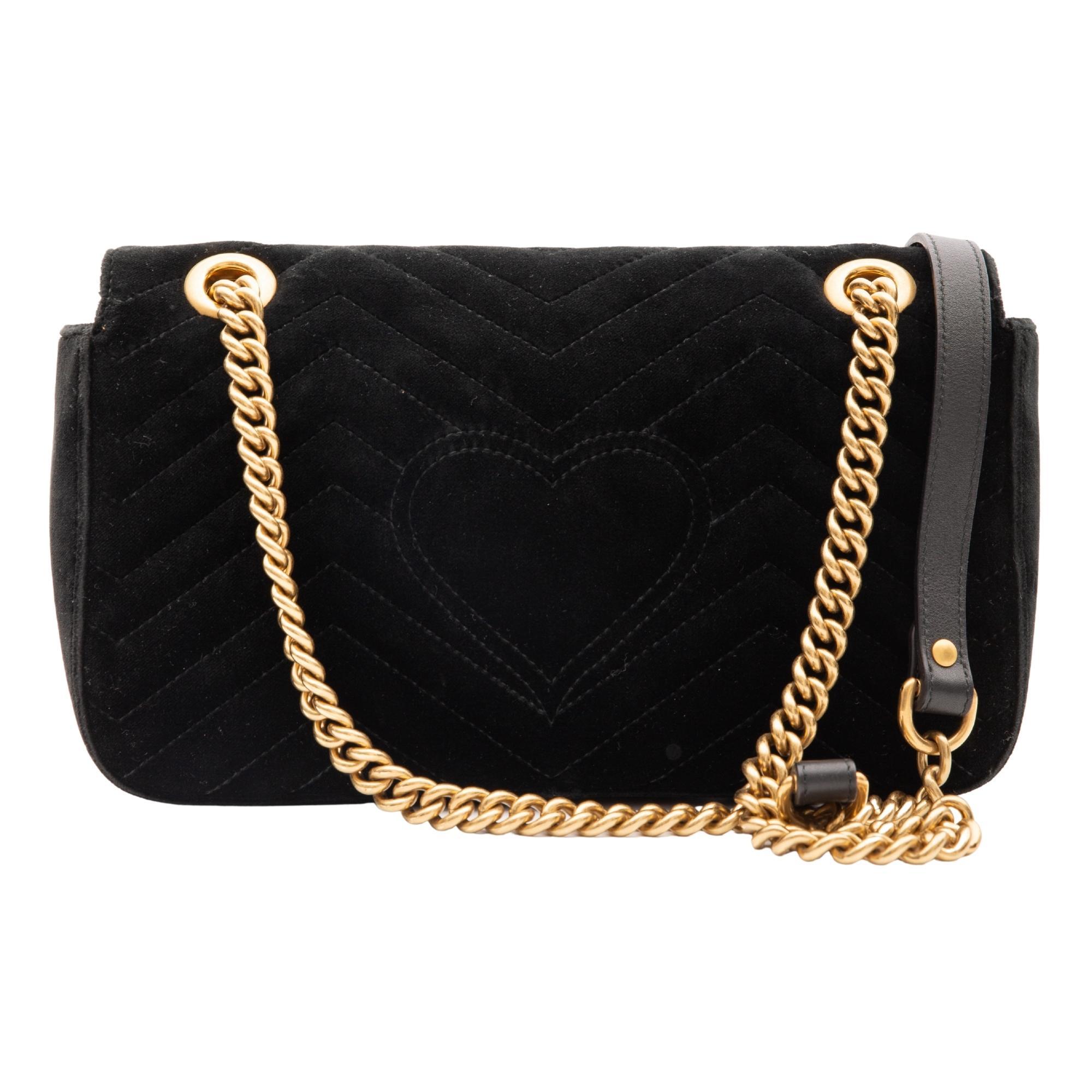 This shoulder bag is made of soft velvet in black. This bag features a long aged gold chain shoulder strap with a leather shoulder pad. The front cross over flap features an interlocking GG logo that opens to a pink satin fabric interior with a