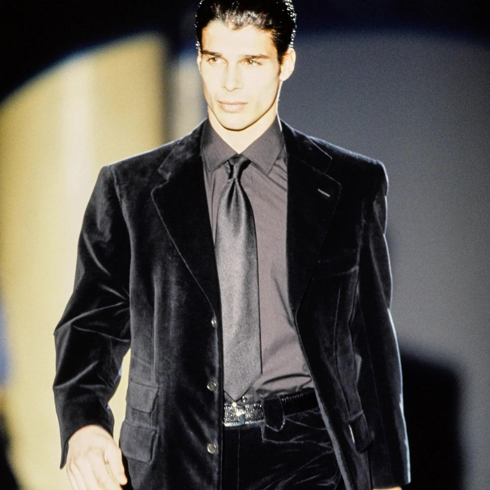 Dall'autunno 1995 di Tom Ford, blazer in velluto grigio in misto cotone e seta con fodera in cupro. Presenta un'elegante chiusura a due bottoni. 
 Osservazioni: Un pulsante è parzialmente rotto. 
 Materiale: 70% cotone 30% seta 
 Misure: