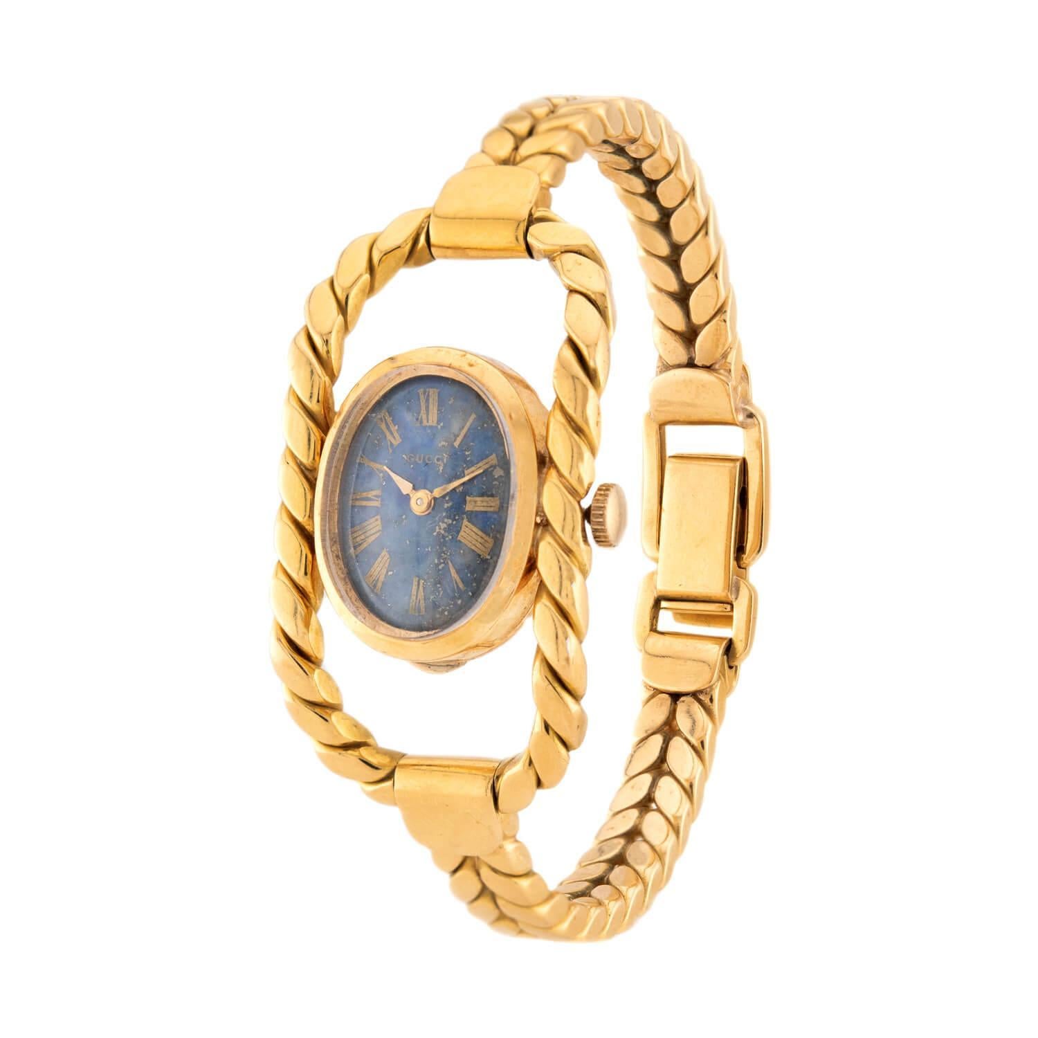 An absolutely stunning Gucci watch from the Vintage (ca1970s) era! Crafted in vibrant 18k yellow gold, this watch features an oval-shaped face. The face of the watch is a deep speckled blue hue, and the Roman numerals, which represent the hours, are