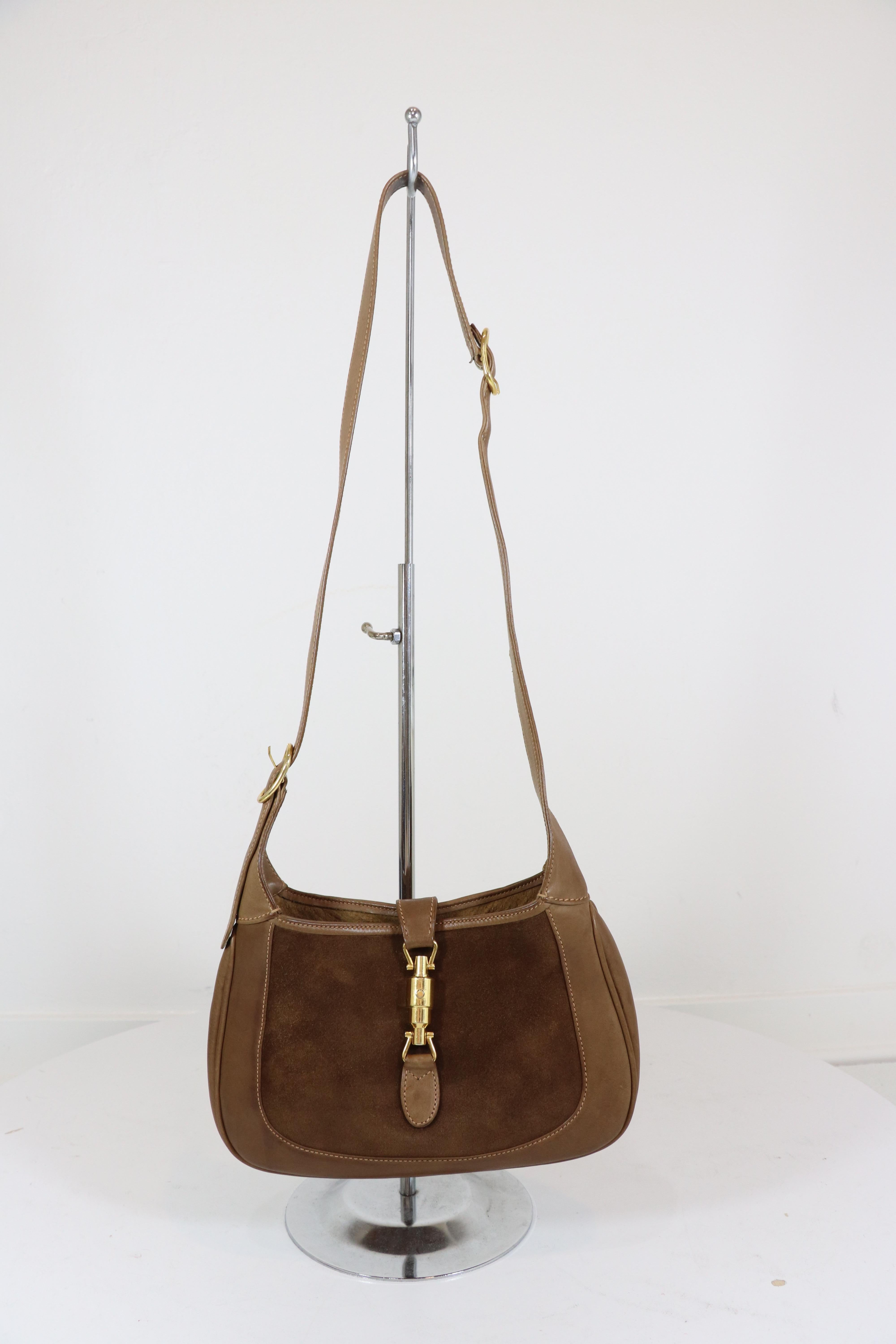 Gucci 1970's vintage small Jackie O bag,  in medium brown suede with brown calf leather trim and handle and a gold-tone piston clasp closure at the front. Interior is fully lined with one zippered pocket. Bag includes a matching leather extension