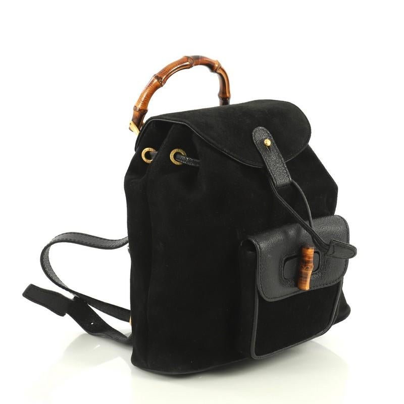 This Gucci Vintage Bamboo Backpack Suede Mini, crafted from black suede, features a bamboo top handle, adjustable backpack straps, leather trim, exterior front pocket with bamboo twist-lock closure, and gold-tone hardware. Its drawstring top flap