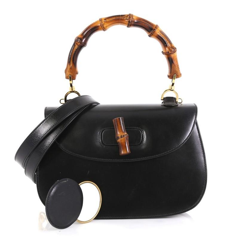 This Gucci Vintage Bamboo Convertible Top Handle Bag Leather Medium, crafted from black leather, features a bamboo top handle and gold-tone hardware. Its bamboo turn-lock closure opens to a red leather interior with side zip and slip pockets.