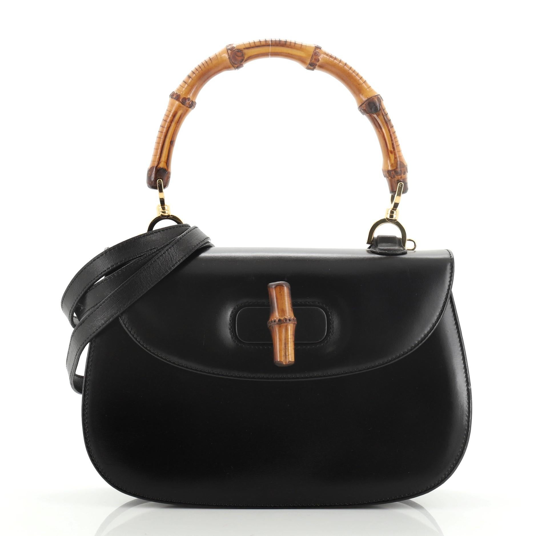 This Gucci Vintage Bamboo Convertible Top Handle Bag Leather Medium, crafted from black leather, features a bamboo top handle and gold-tone hardware. Its bamboo turn-lock closure opens to a red leather interior with side zip and slip pockets.