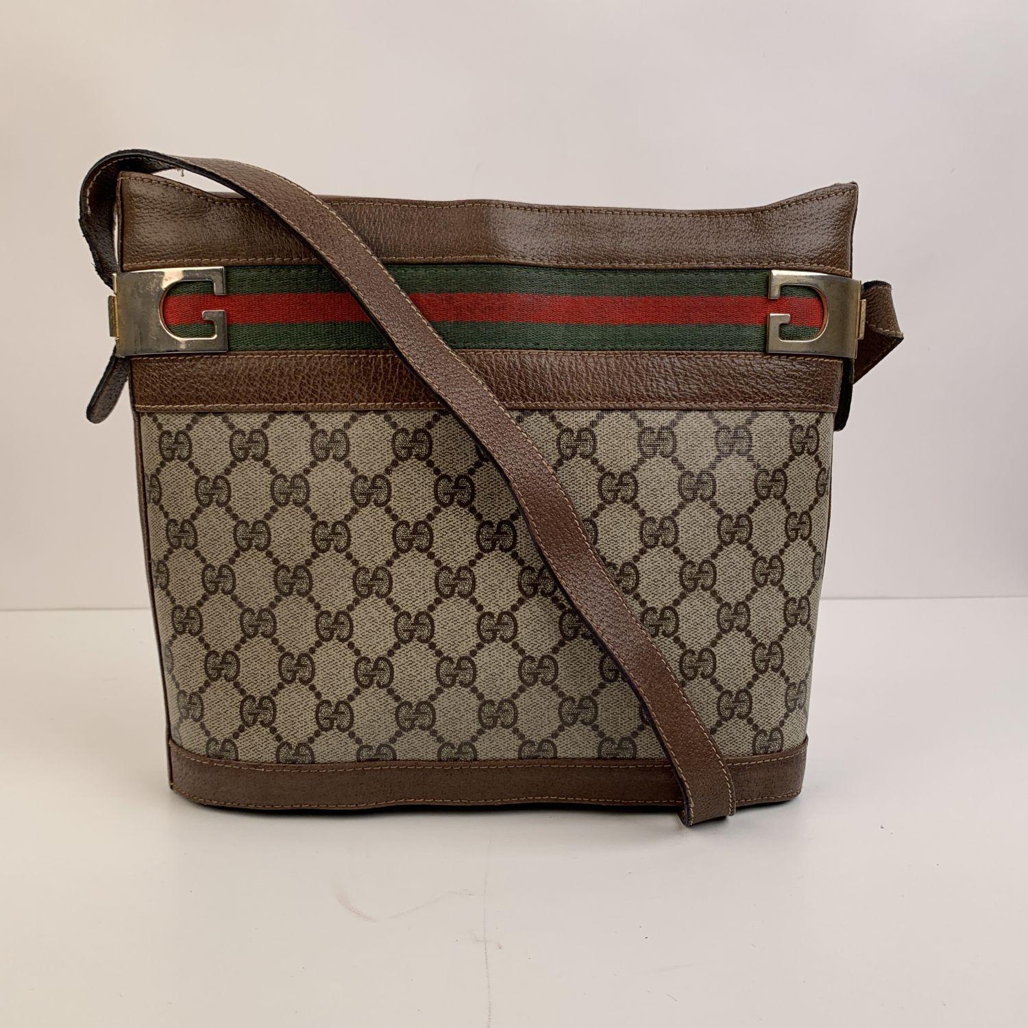 Vintage Gucci bucket shoulder bag crafted in beige monogram canvas with genuine leather trim and strap. Green/Red/Green striped detailing on the upper part of the bag. G-shaped hardware in gold-tone metal. Magnetic button closure on top and