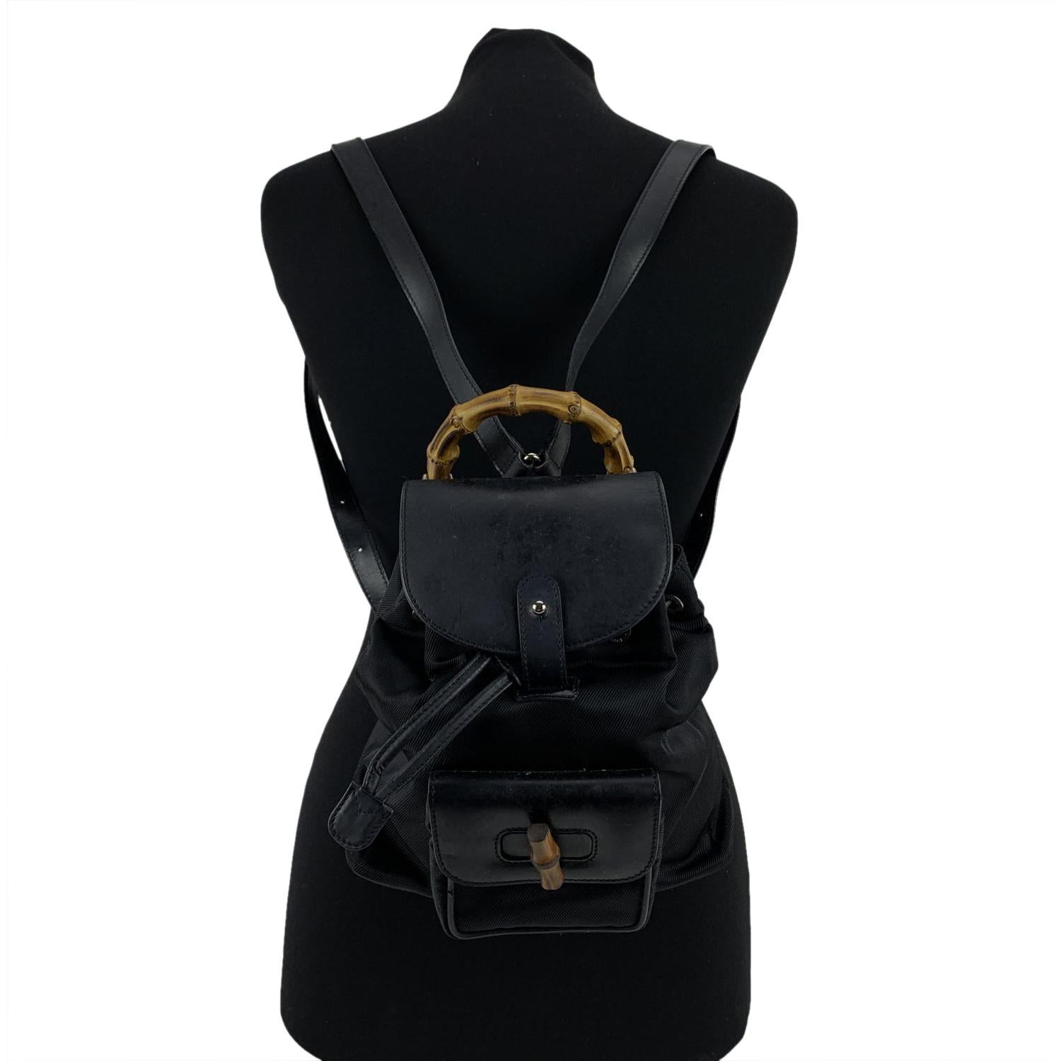 Vintage small backpack by Gucci, crafted in black canvas and leather. It features Bamboo handle and and knob. 1 front pocket with twist lock closure. Flap closure and drawstring top opening. gold metal hardware. Internal diamond lining. 1 side zip