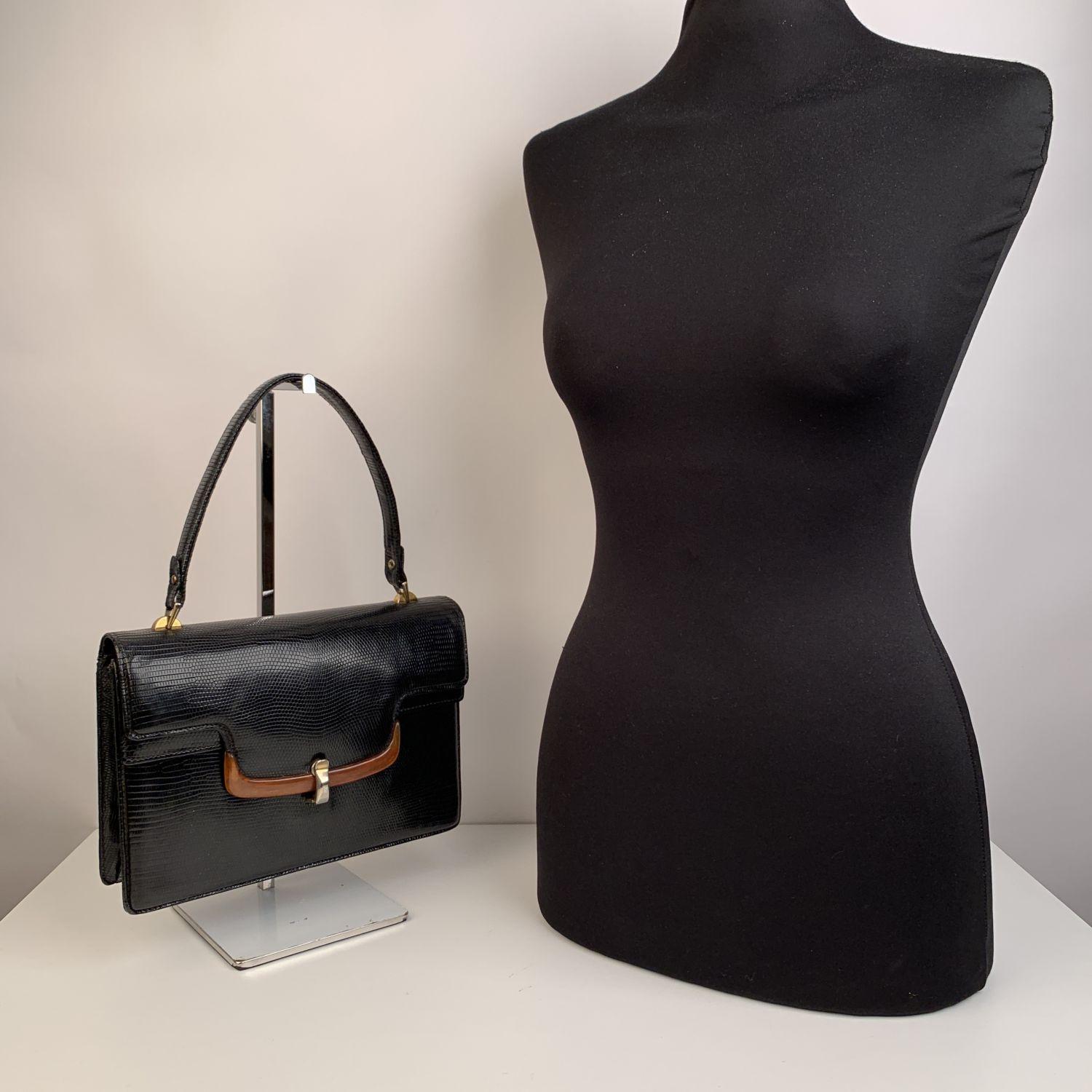 Elegant black lizard leather vintage handbag from the 1960s by GUCCI. the bag features a bakelite detail to the front. Gold metal hardware. Flap with front clasp closure. 1 flap section under the main flap on the front. 1 rear open pocket. Black