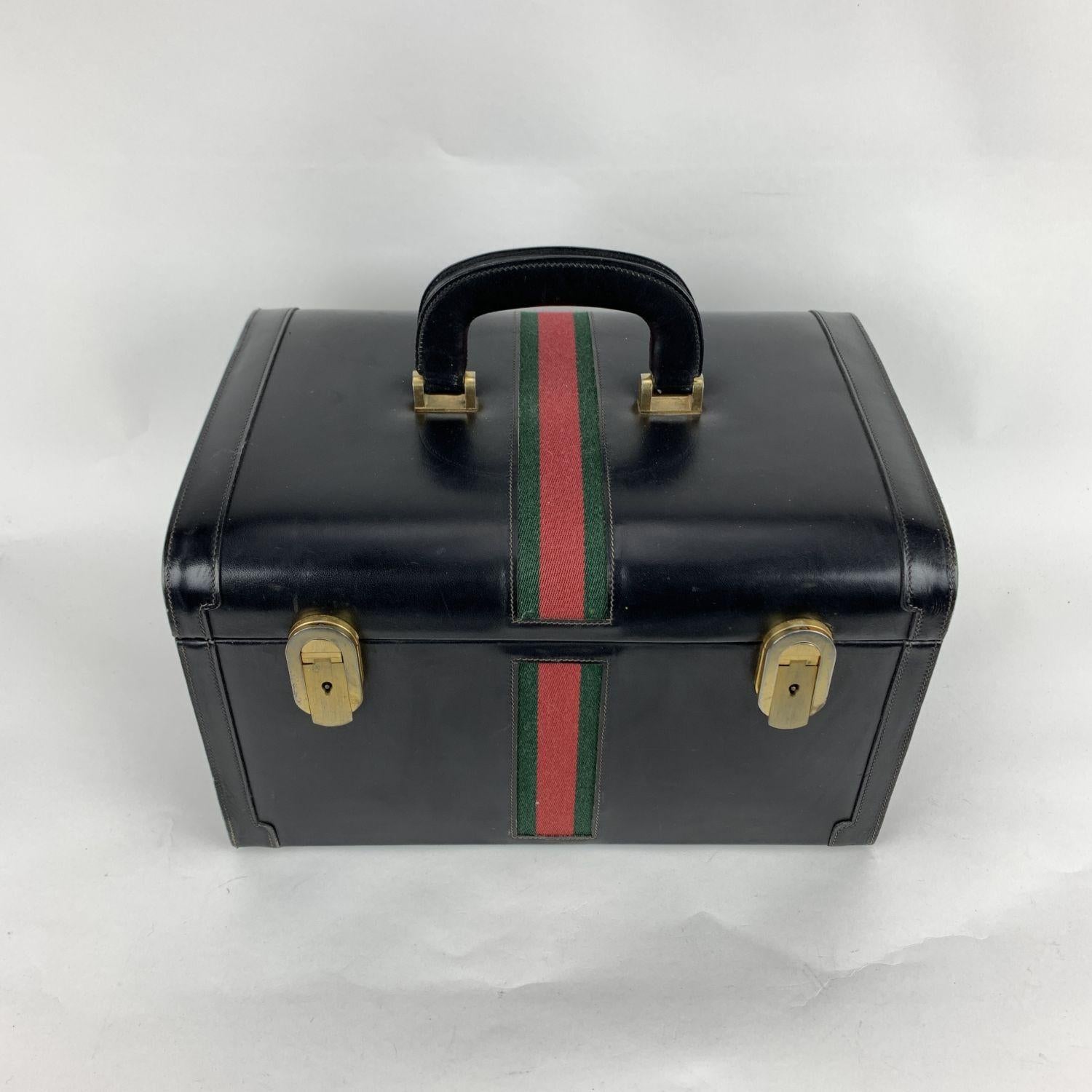 Splendid vintage train case by GUCCI, from the early 1970s. Crafted in black leather. It features green/red/green striped detailing and gold-tone metal hardware. Double key lock closure (keys are included). Beige leather internal lining. 1 removable