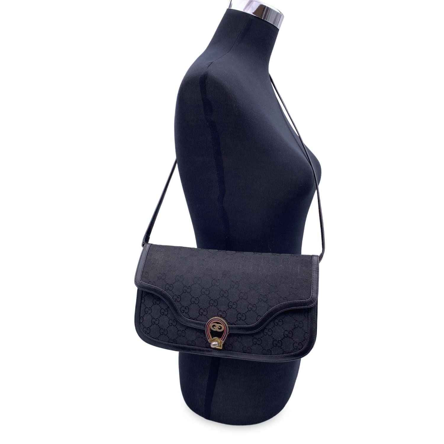 Gucci vintage shoulder bag in black monogram canvas with black leather trim and shoulder strap. GG - Gucci logo on the front with red and green enamels. Convertible model. It can be used as a shoulder bag or as a clutch purse if you remove its