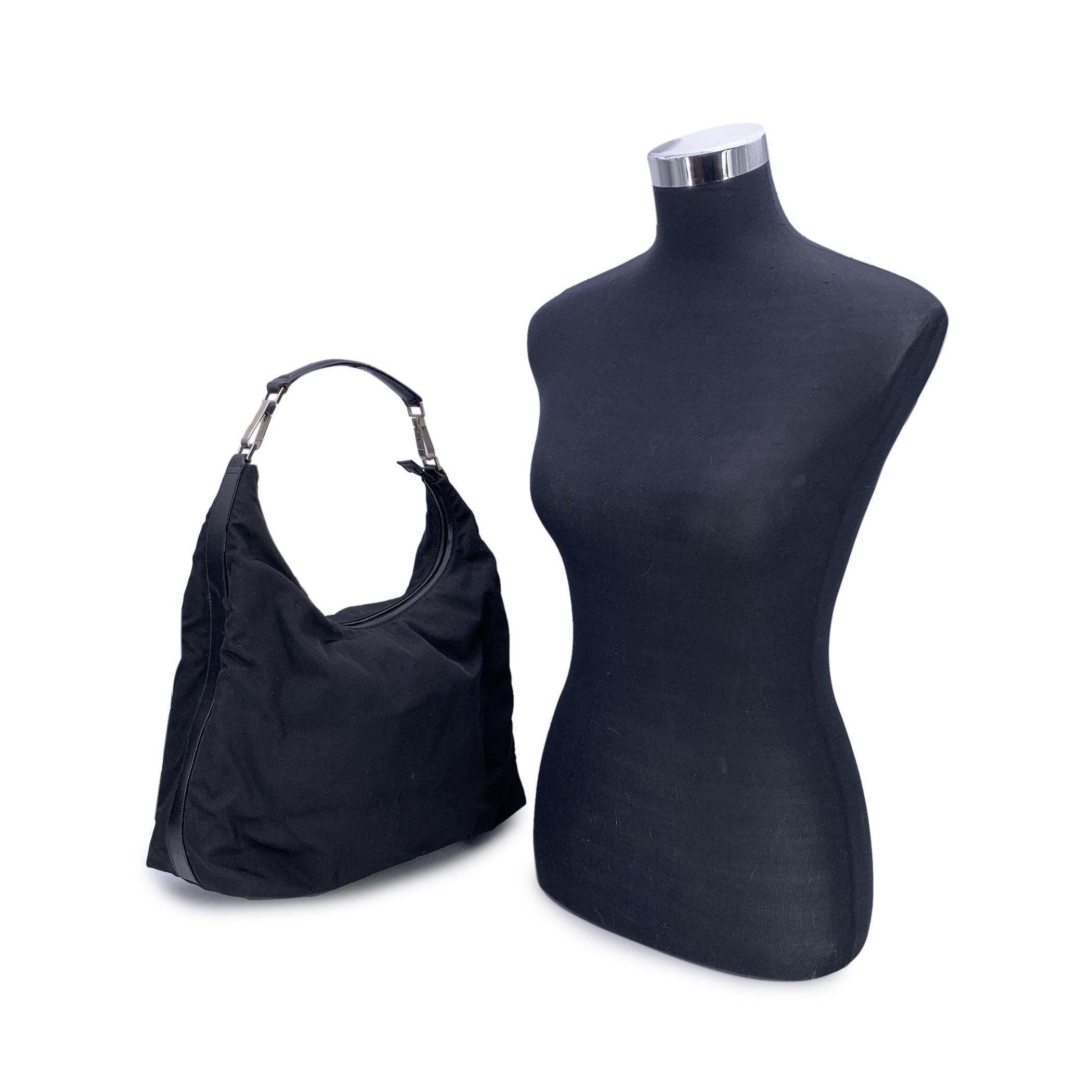 Elegante y minimalista sin esfuerzo, este bolso hobo vintage de Gucci está confeccionado en lona de nailon negra y acabado con ribetes y asa de piel negra: una mezcla atemporal de elegancia informal y diseño italiano icónico. Los herrajes en tono