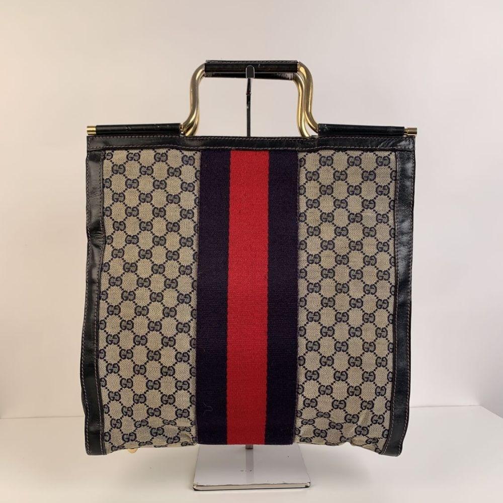 Beautiful Gucci tote made in blue monogram canvas with blue leather trim. Blue/Red/Blue stripes on the front and on the back. Metal handles. Open top. Velvet lining. 1 side zip pocket inside. 'Made in Italy by GUCCI' embossed