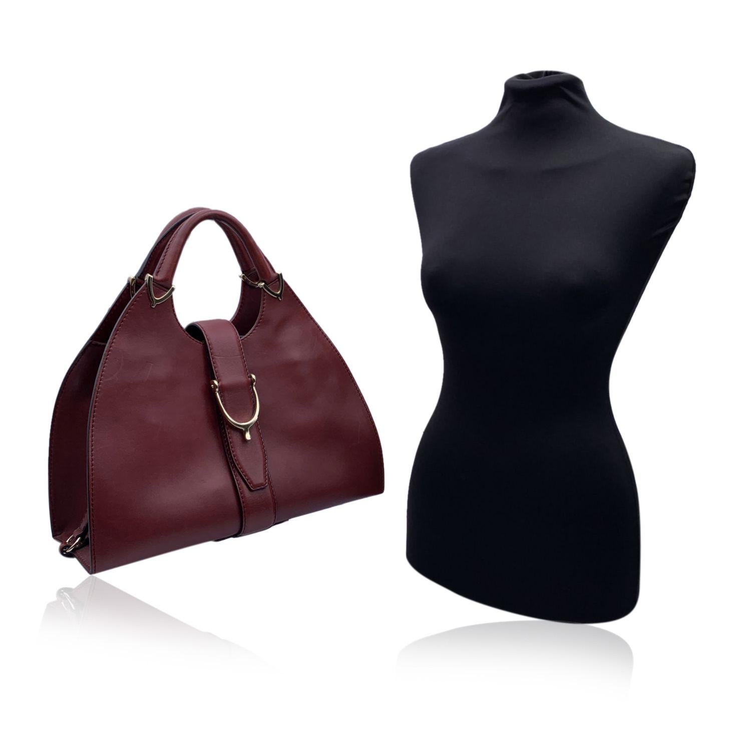 Beautiful Gucci 'Stirrup' hobo bag, crafted in burgundy leather. Light gold hardware. Fold over strap with button closure. Spur detailing on the front and on the handles. Canvas interior with 1 side zip pocket inside and 3 side open pockets. Gucci