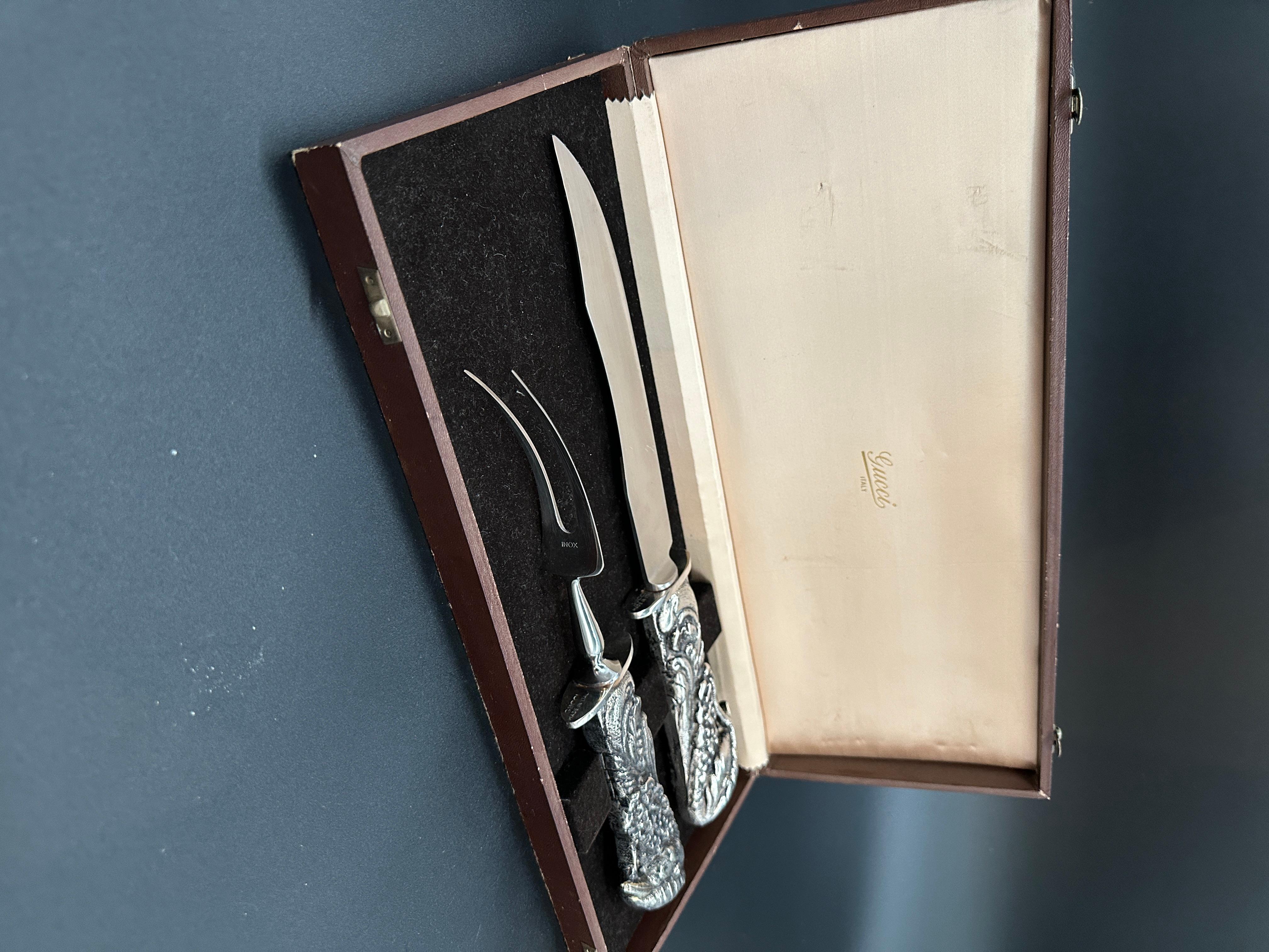 Gucci carving set, consisting of a carving knife and a two-pronged fork, housed in a fitted case. The case is lined with velvet at the base and satin on the lid, where the 