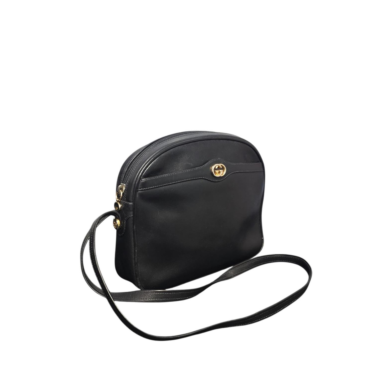 The Gucci Vintage GG Leather Camera Shoulder Bag is crafted from smooth black leather with elegant gold-tone hardware, embodying timeless luxury. Made in Italy, it features a 19” flat shoulder strap for comfortable wear and a single top zipper
