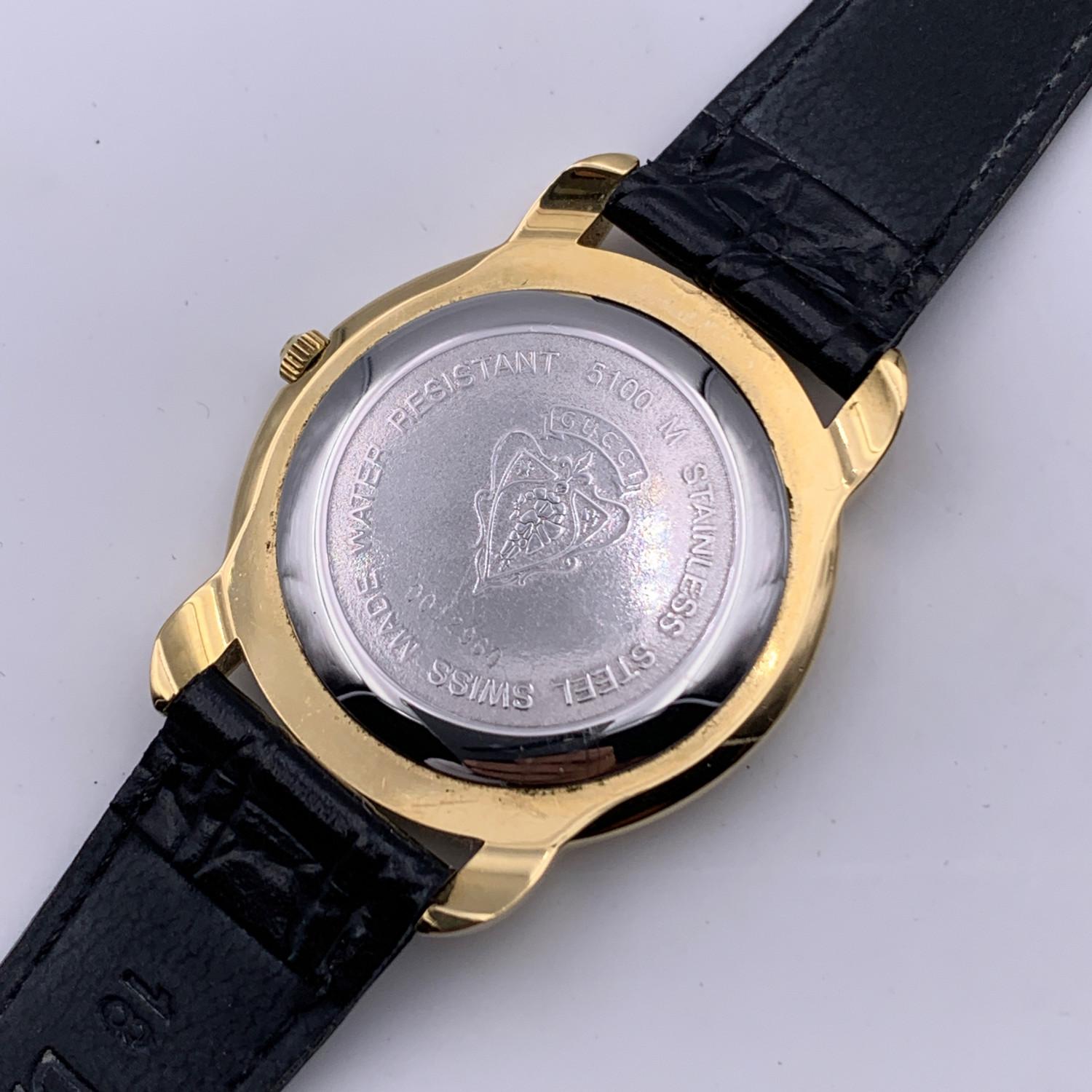 Beautiful vintage wristwatch mod. 5100 M by GUCCI. Round gold metal stainless steel case. Black dial. Swiss Made Quartz Movement. Roman numbers around the bezel. Date indicator at 6 o clock. Black leather wrist strap with 7 holes adjustment. GG -