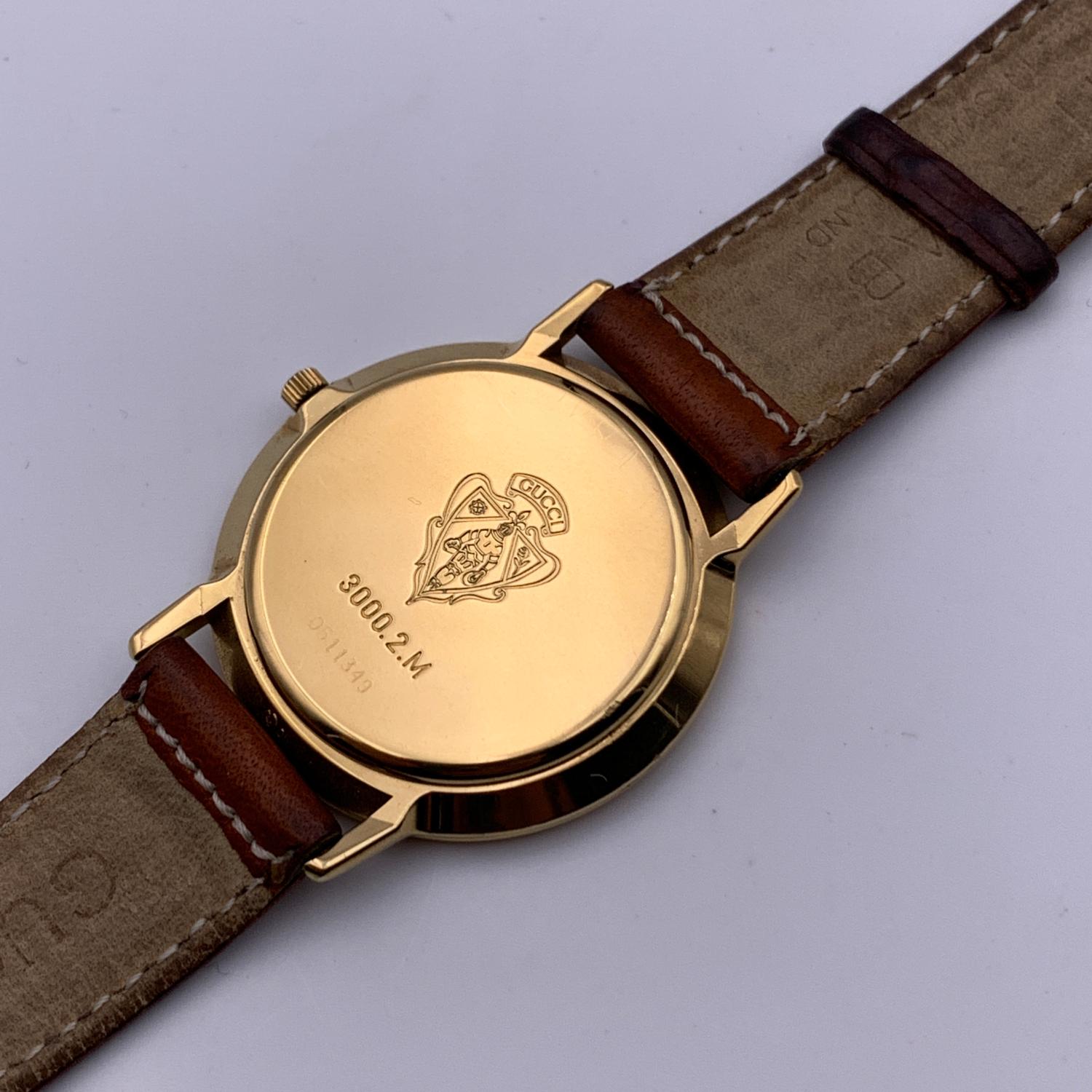 Beautiful vintage wristwatch by GUCCI. Round gold metal stainless steel case. White dial, outer seconds rim and black hands. Swiss Made Quartz Movement. Brown leather wrist strap with 6 holes adjustment. GG - GUCCI buckle. Roman numbers engraved on