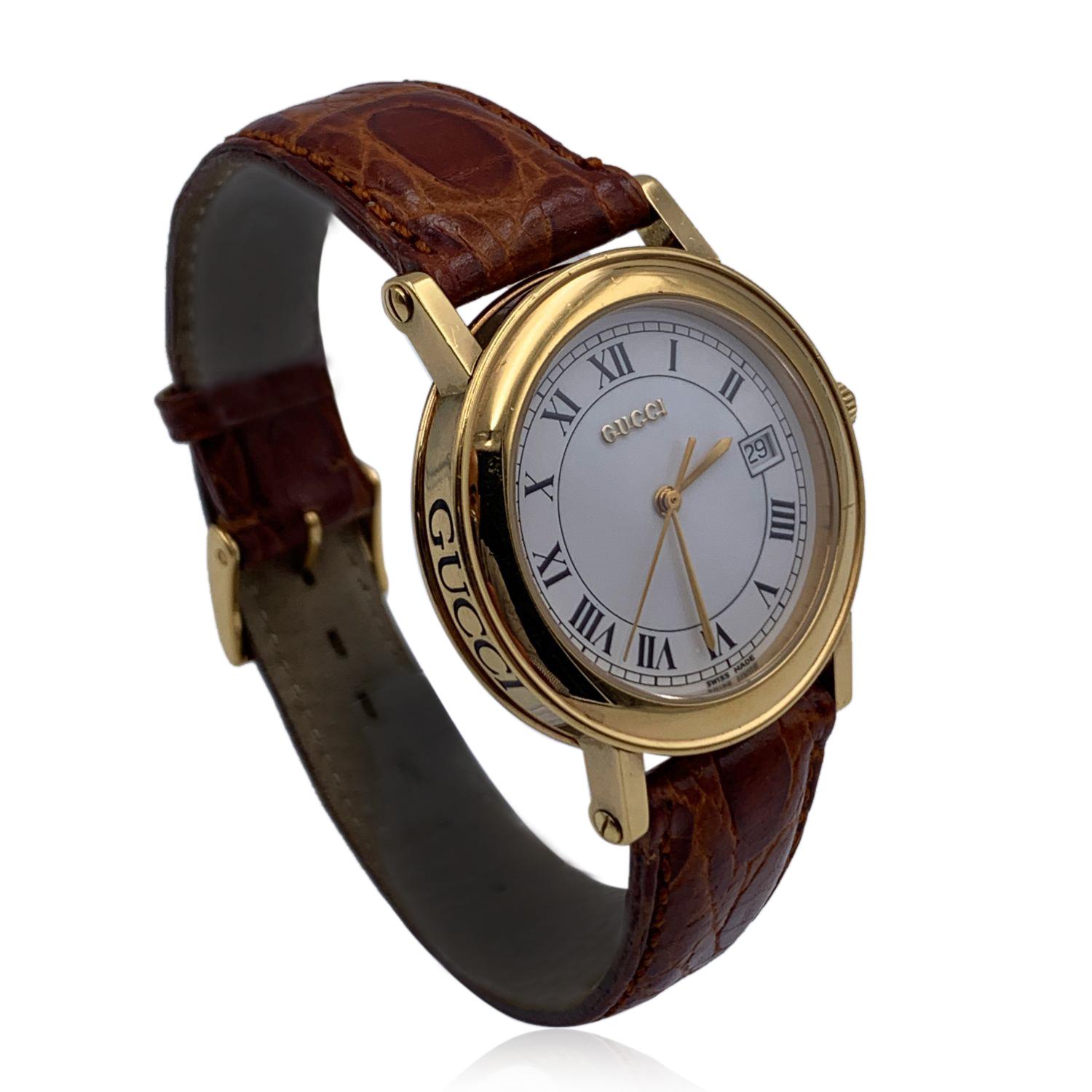Beautiful vintage wristwatch by GUCCI. Round gold metal stainless steel case. White tone dial. Swiss Made Quartz Movement. Brown leather wrist strap with 7 holes adjustment. GG - GUCCI buckle. Roman numbers. Date indicator at 3 o'clock. 'GUCCI'