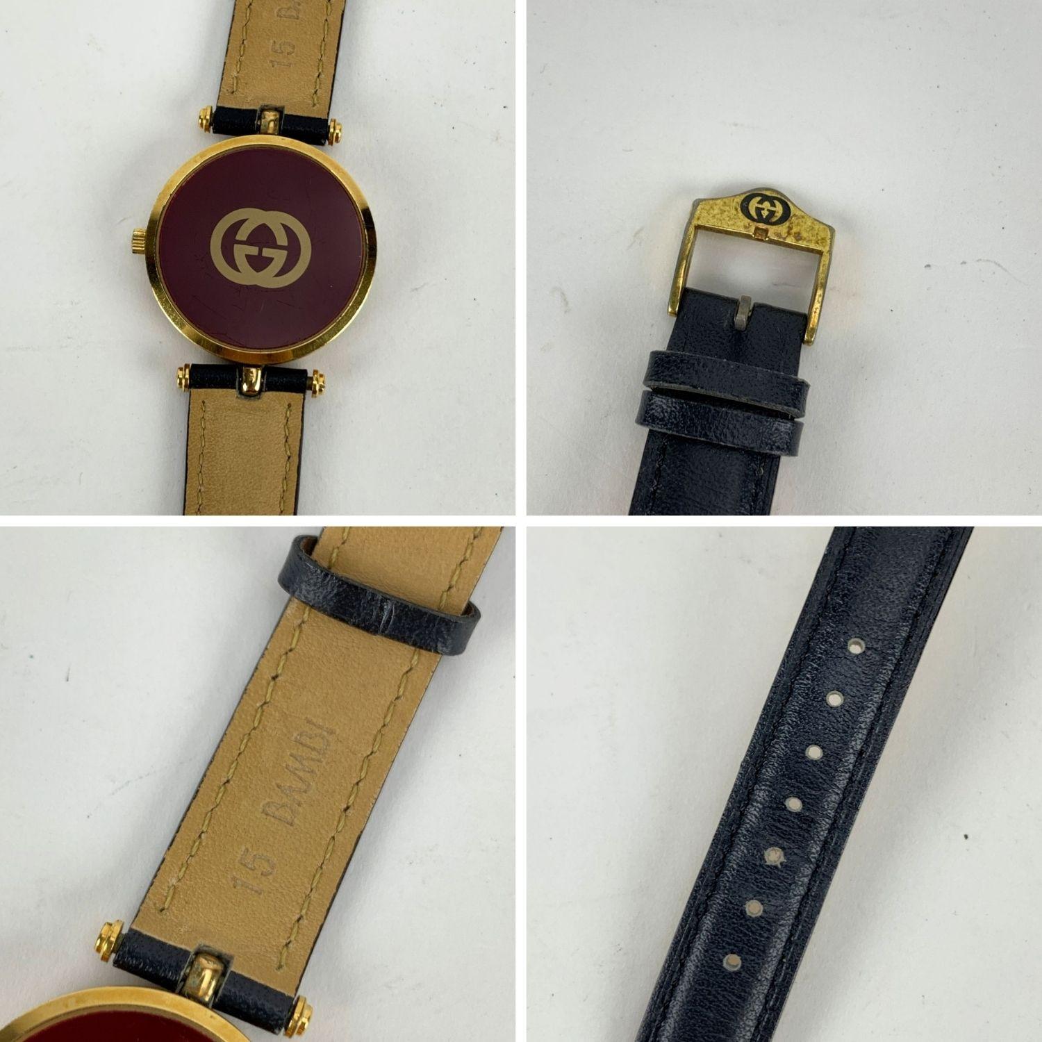 Beautiful vintage wristwatch by GUCCI. Round gold metal stainless steel case. Green/Red/Green stripes around the case. Gold tone dial. Swiss Made Quartz Movement. Black leather wrist strap with 7 holse adjustment. GG - GUGGI buckle. Roman numbers.