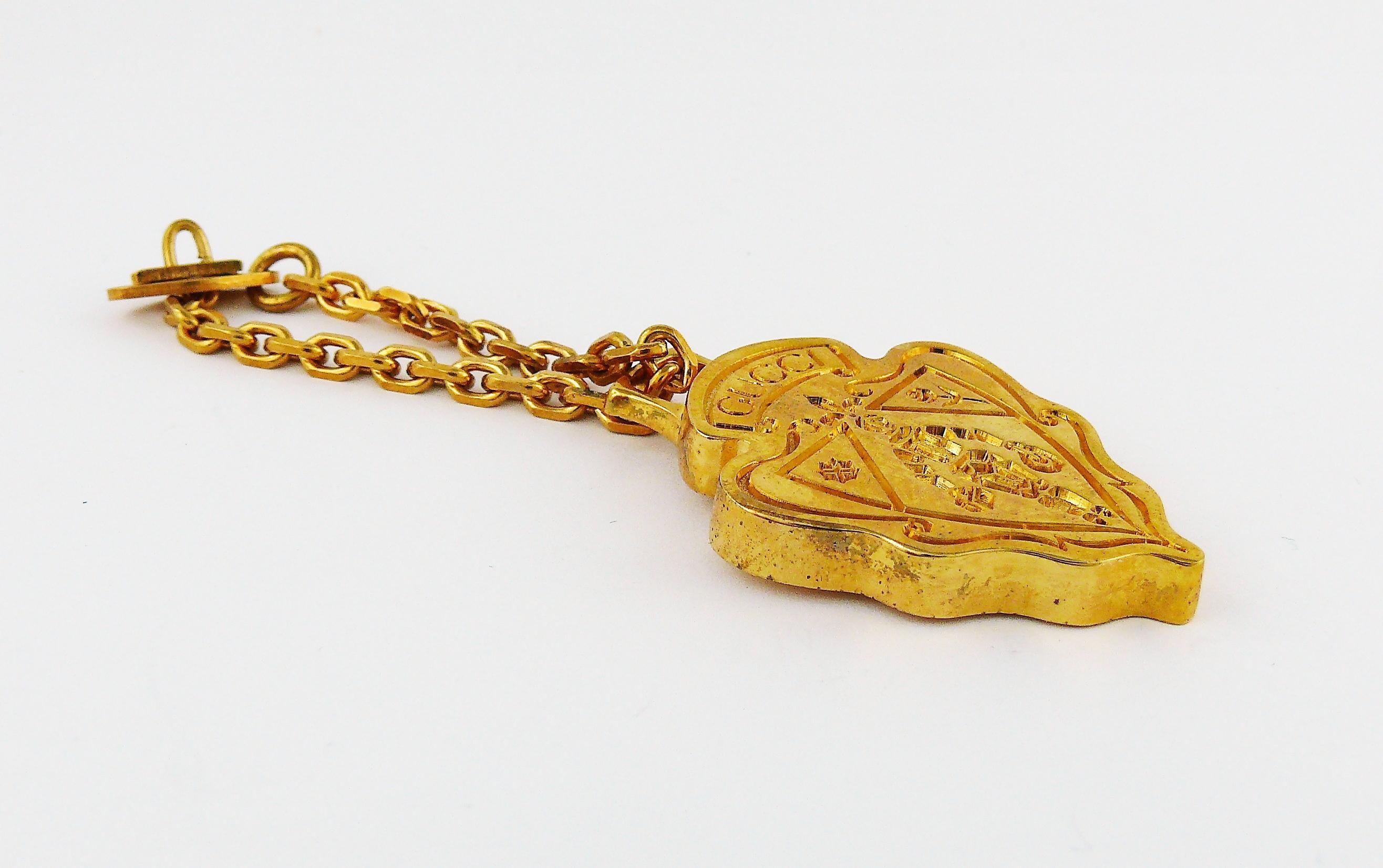 GUCCI Parfums goldfarbenes Accessoire mit Wappen.

Kann zum Beispiel als Schlüsselanhänger oder Taschenanhänger verwendet werden.

Dieses Wappen wurde ursprünglich mit dem Duft GUCCI NOBILE parfümiert. 

GUCCI-Prägung auf der Vorderseite.
Auf der