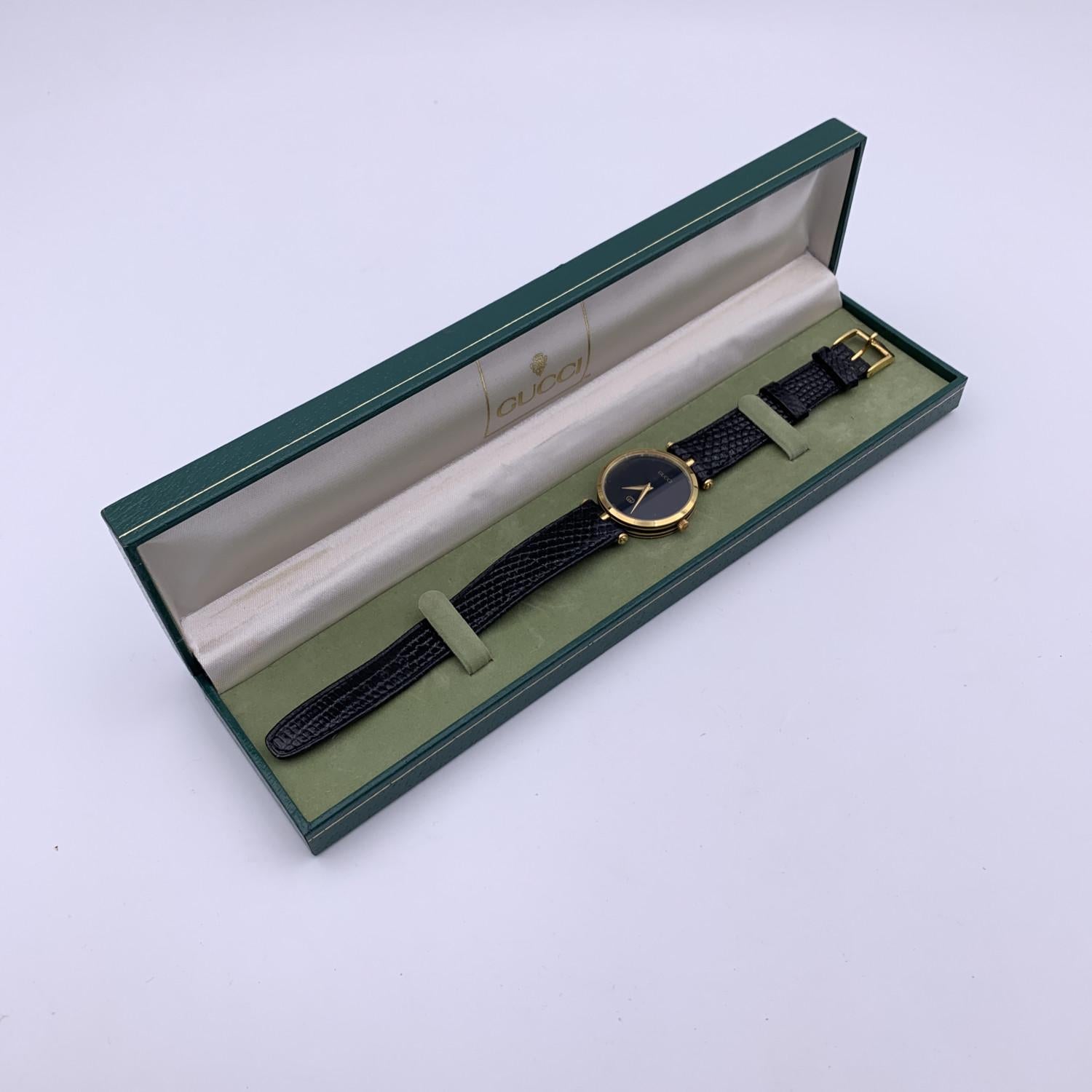 Beautiful vintage wristwatch by GUCCI. Round gold metal stainless steel case. Black enameled stripes around the case. Black dial. Swiss Made Quartz Movement. Black leather wrist strap with 6 holes adjustment. GG - GUCCI buckle. 'GUCCI' lettering on