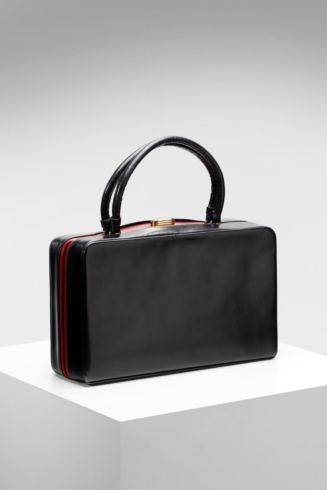 Elegant fine handbag from the great Italian fashion house Gucci from the 1950s-60s. The model shown is a small, rigid, double-handled handbag bauletto. Made of black leather conn central inserts in fiery red leather. Its closure is in gold metal .