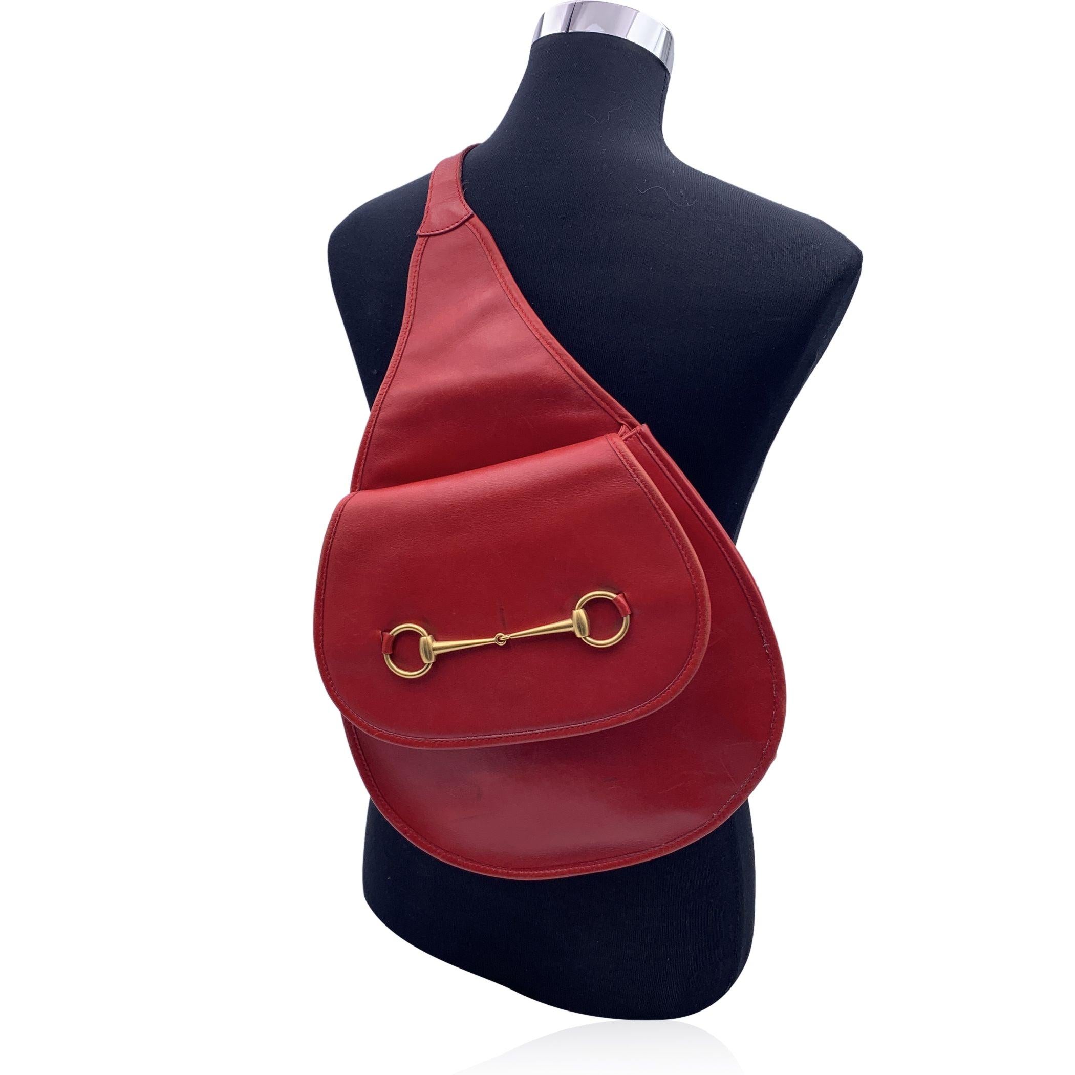 Rare vintage sling shoulder bag backpack by Gucci, crafted in red leather. It features gold metal horsebit on the front. Flap with magnetic button closure on the front. Internal diamond lining. 1 side zip pocket inside. Single convertible flat