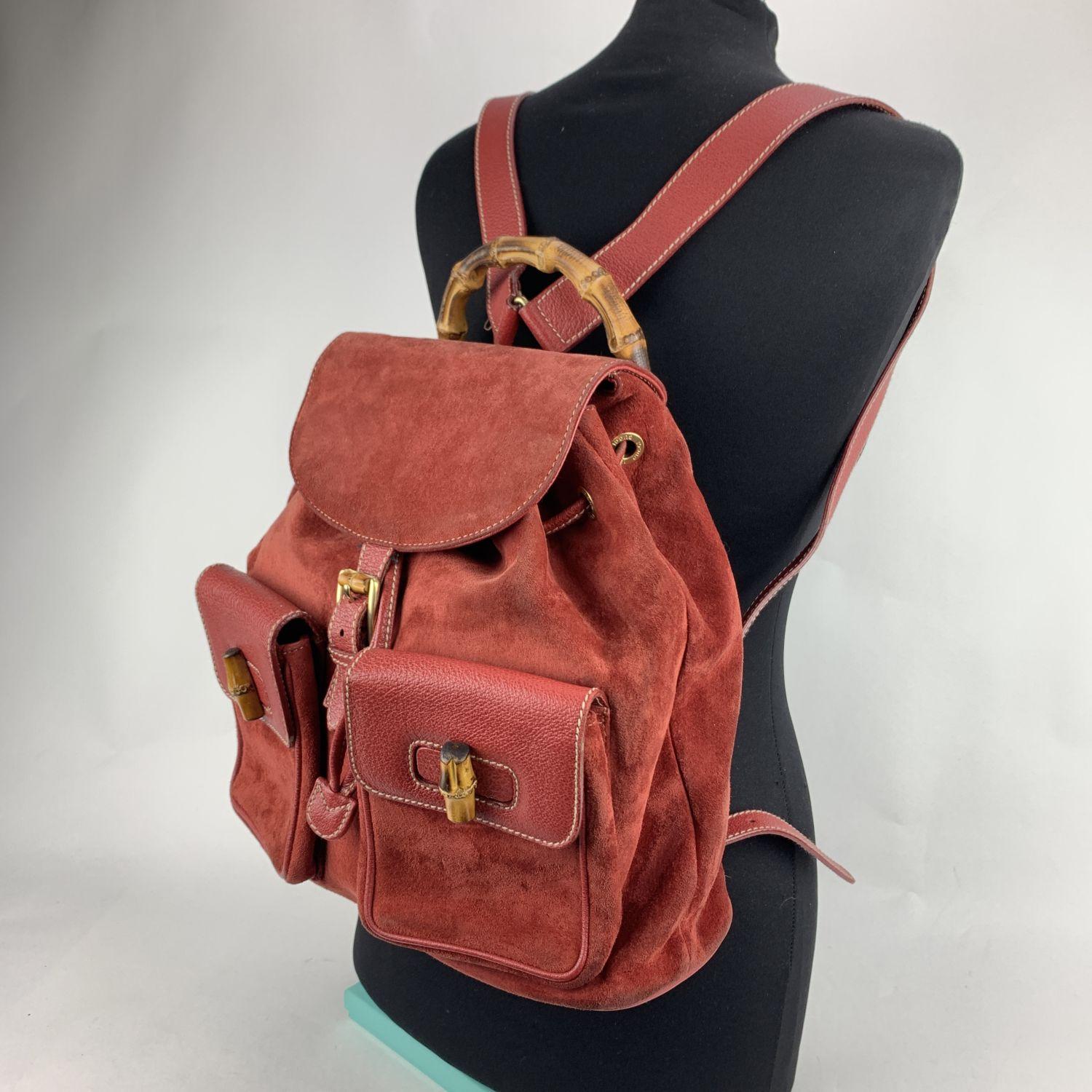 Vintage backpack by Gucci, crafted in red suede and leather. It features Bamboo handle and knobs. 2 front flap pockets.Flap with buckle closure and drawstring top opening. Internal beige diamond lining. 1 side zipper pocket inside (GUCCI - GG gold