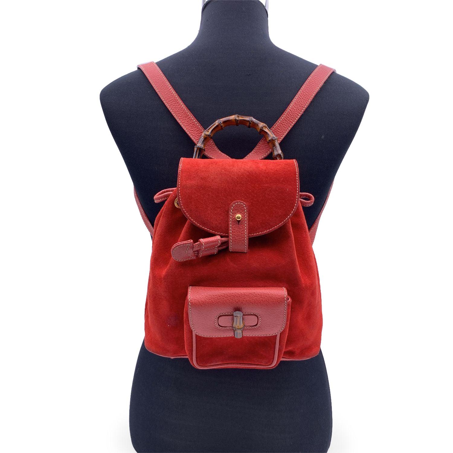 Vintage small backpack by Gucci, crafted in red suede and leather. It features Bamboo handle and and knob. 1 front pocket with twist lock closure. Flap closure and drawstring top opening. Gold metal hardware. Internal diamond lining. 1 side zip