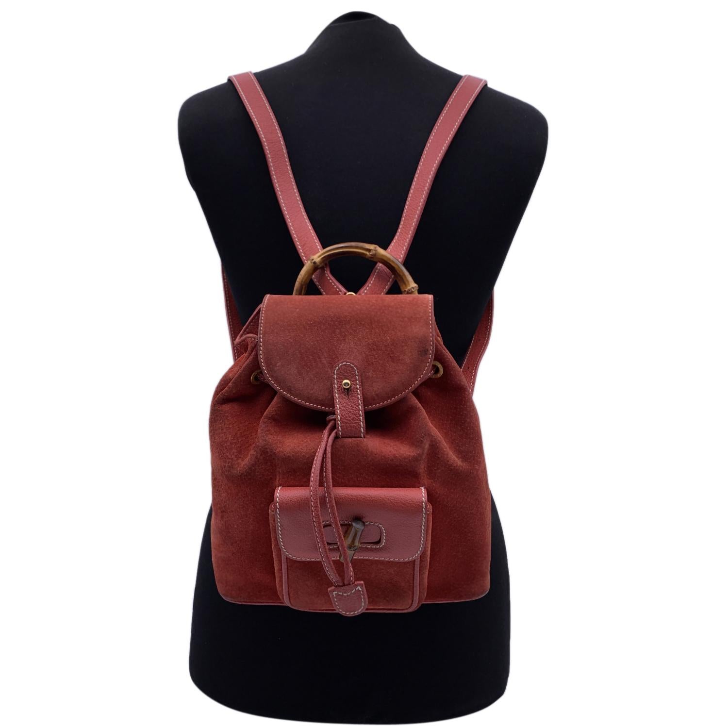 Vintage small backpack by Gucci, crafted in red suede and leather. It features Bamboo handle and and knob. 1 front pocket with twist lock closure. Flap closure and drawstring top opening. gold metal hardware. Internal beige diamond lining. 1 side