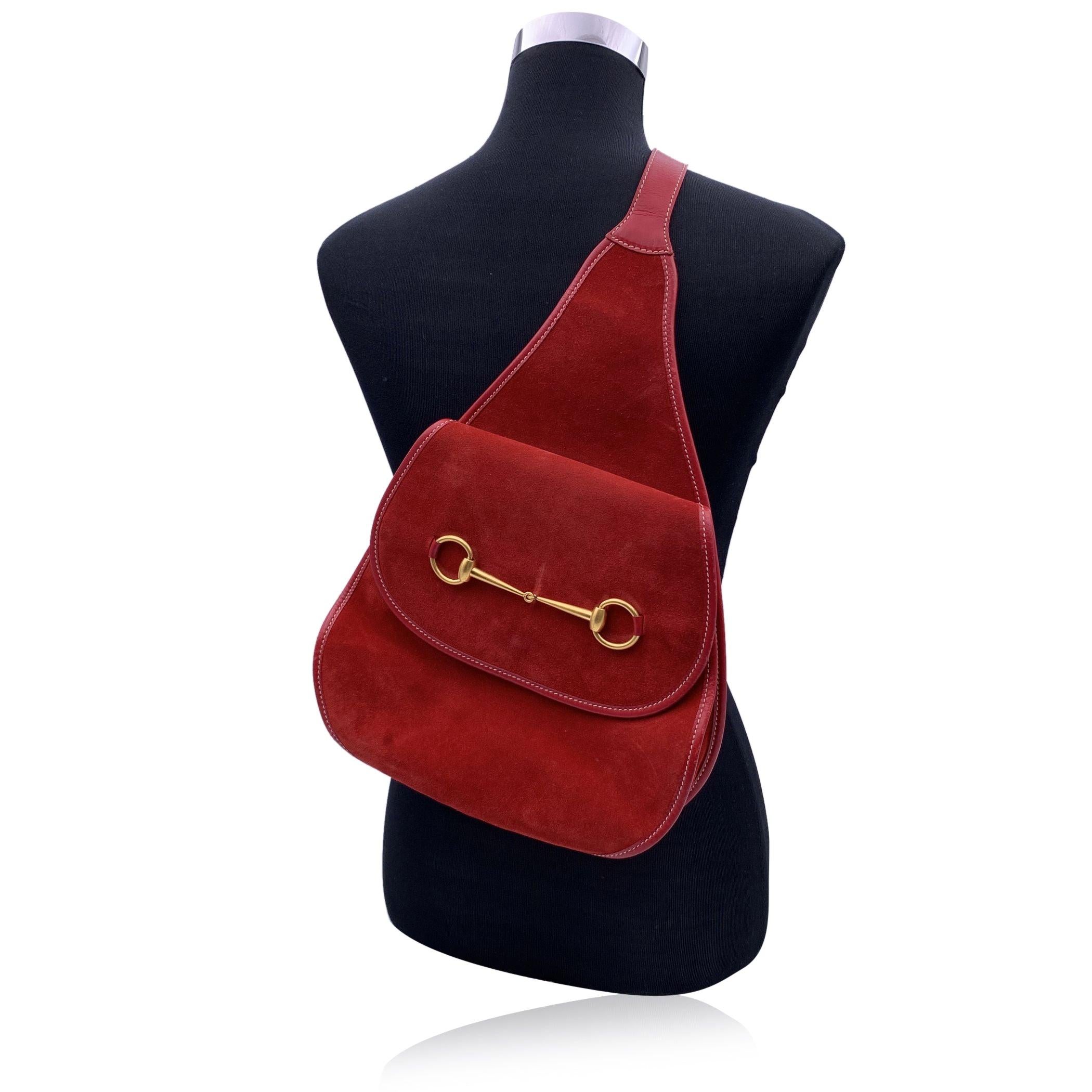 Rare vintage sling shoulder bag backpack by Gucci, crafted in red suede and leather. It features gold metal horsebit on the front. Flap with magnetic button closure on the front. Internal diamond lining. 1 side zip pocket inside. Single convertible