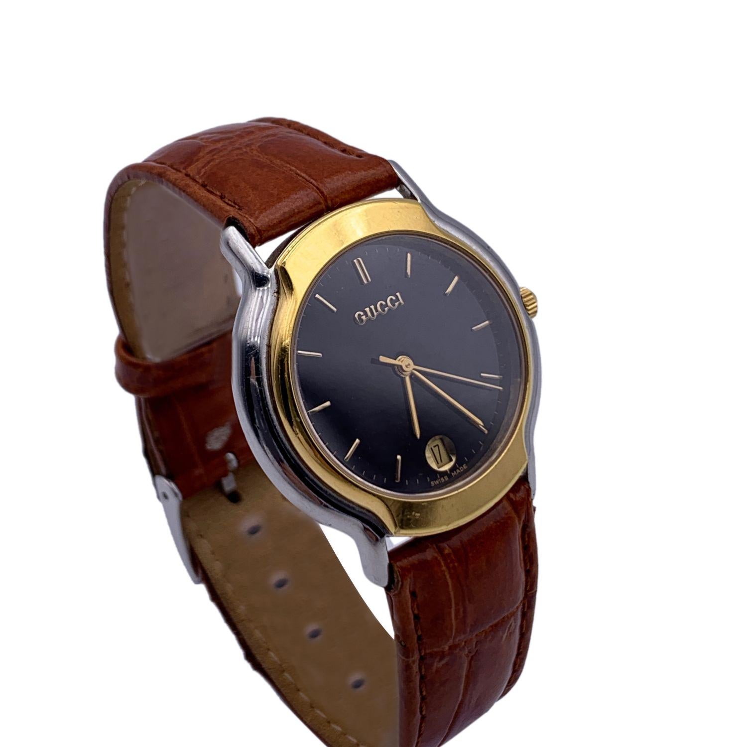 Gucci stainless steel wrist watch, mod. 8000.2 M. Stainless steel case. Gold and silver tonecolors. Black Dial. Date at 6 o'clock. Sapphire crystal. Swiss Made. Quartz movement. Gucci written on face. Gucci crest on the reverse of the case. Water