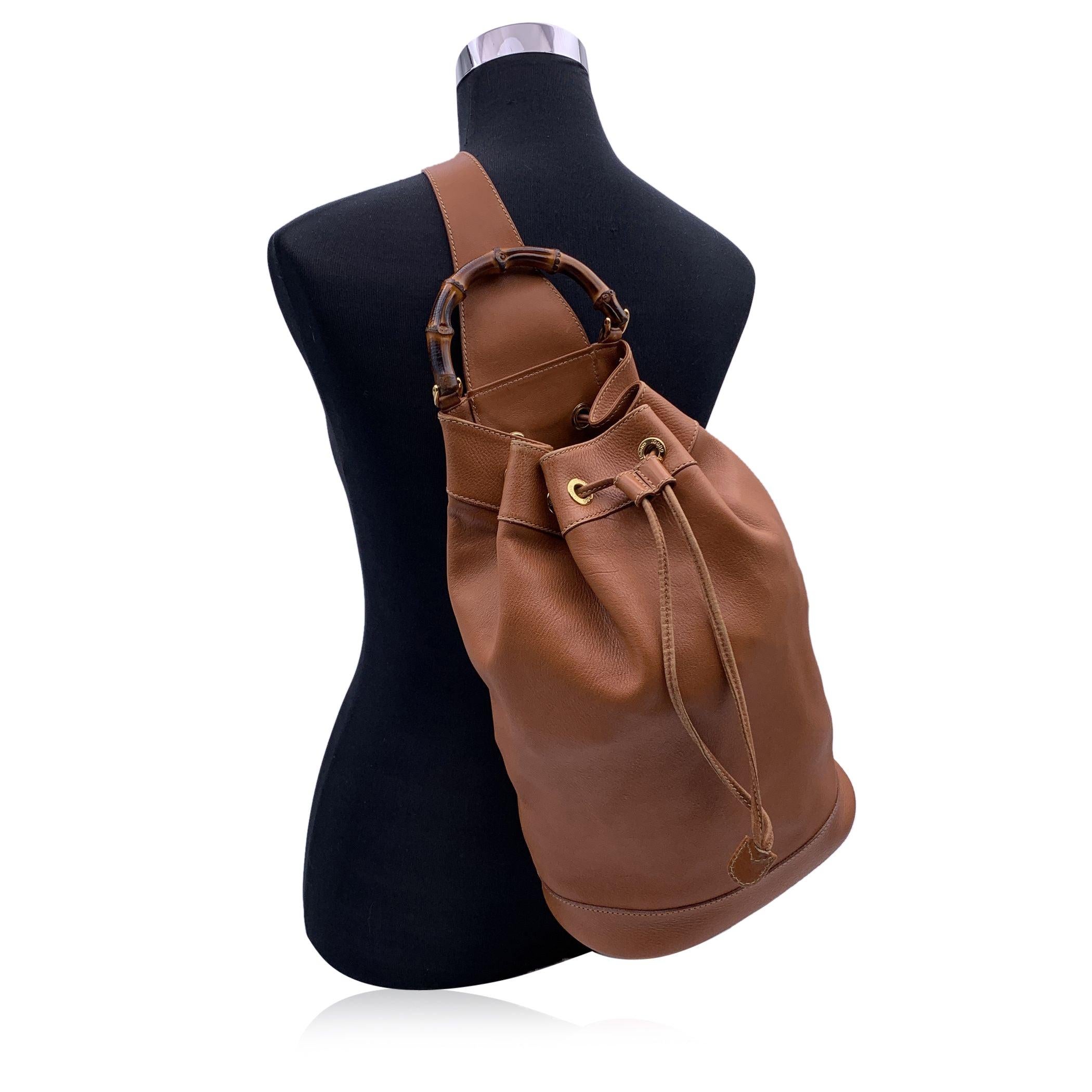 Vintage GUCCI bucket one shoulder backpack is crafted of soft smooth calfskin leather in tan color. It features gold metal hardware and a bamboo handle. Drawstring closure on top. Unlined interior with a detachable zippered pouch. Adjustable