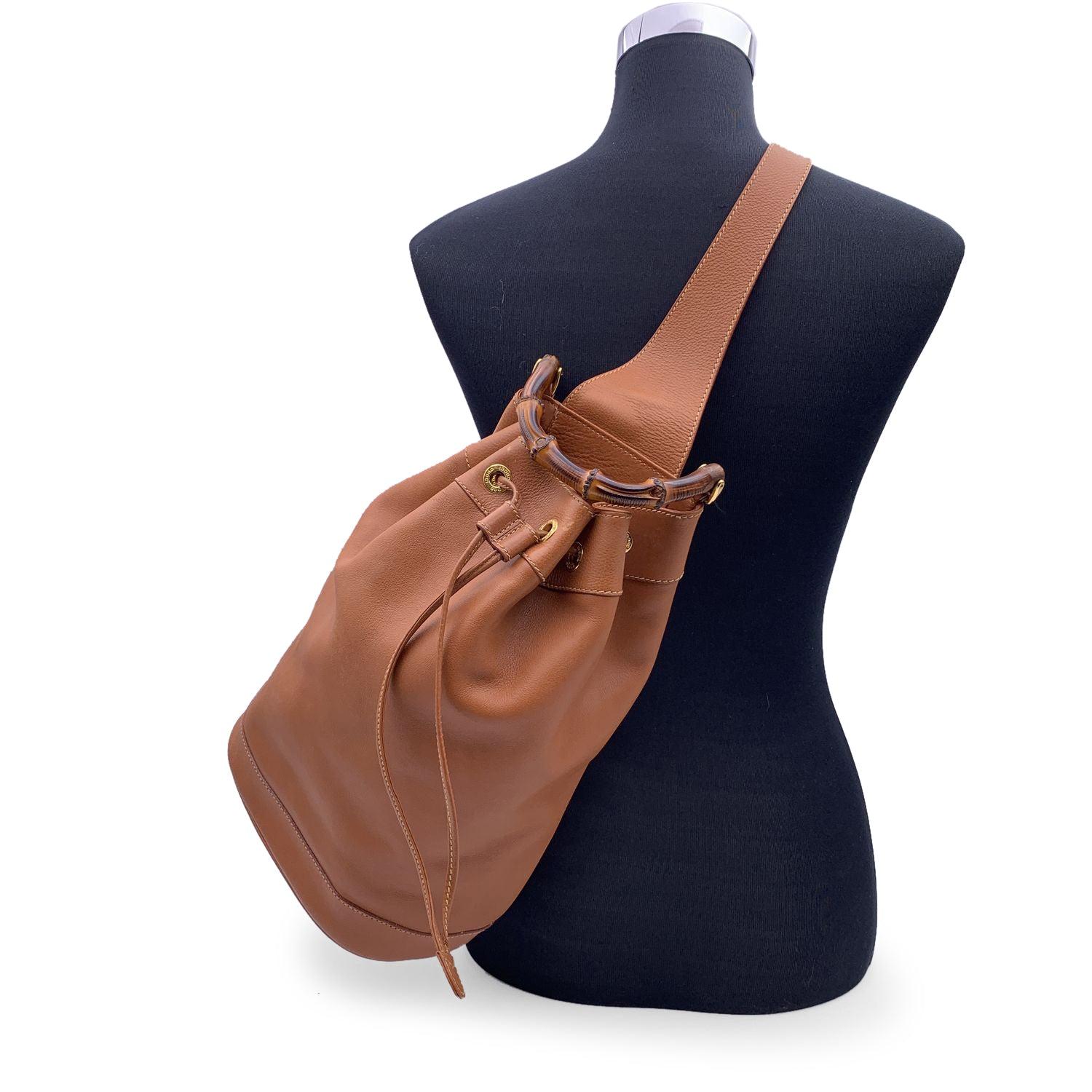 Vintage GUCCI bucket one shoulder backpack is crafted of soft smooth calfskin leather in tan color. It features gold metal hardware and a bamboo handle. Drawstring closure on top. Unlined interior with a detachable zippered pouch. Adjustable