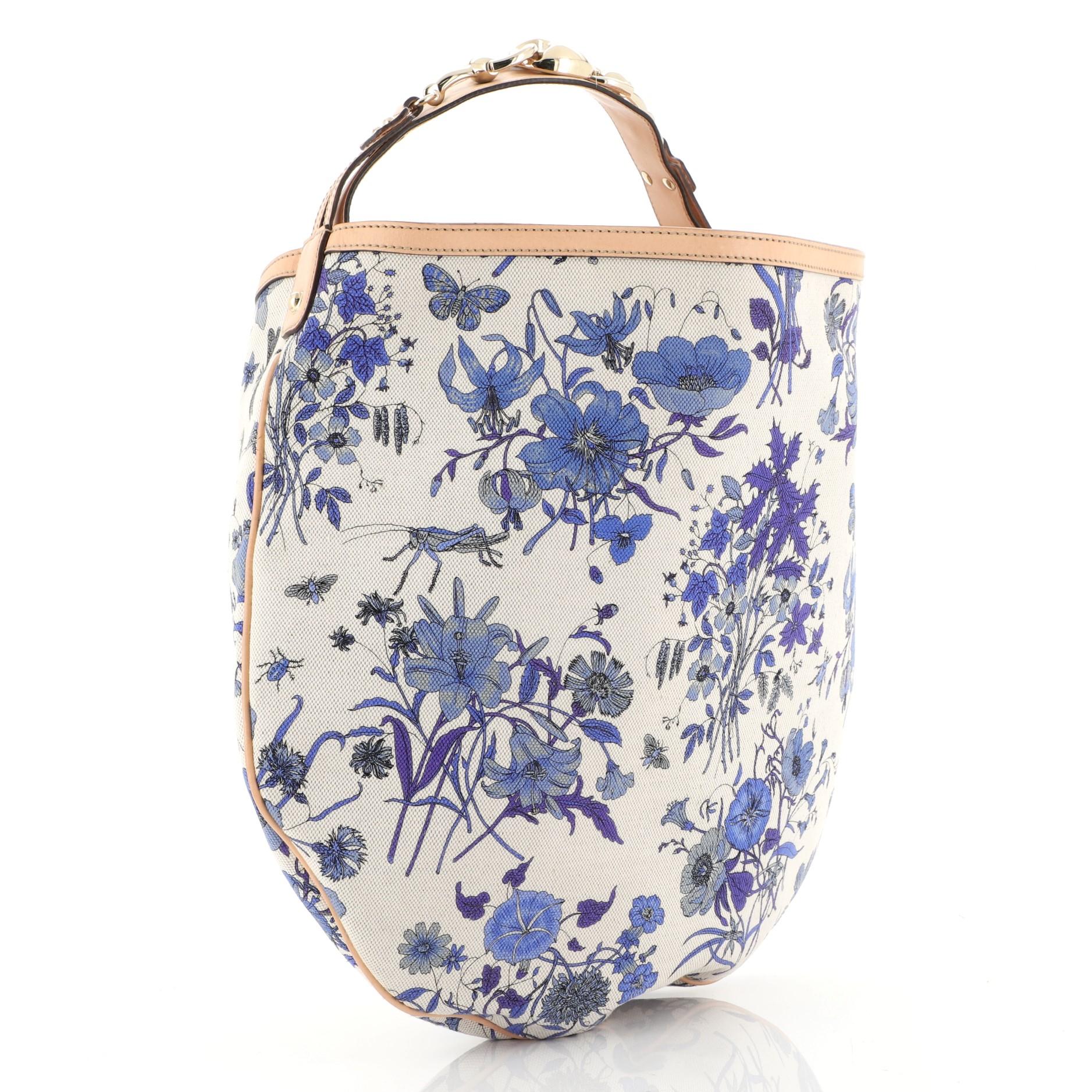 This Gucci Wave Hobo Flora Canvas, crafted from a blue floral printed canvas, features flat leather shoulder strap with horsebit details, leather trim, and gold-tone hardware. It opens to a neutral fabric interior with side zip and slip pockets.