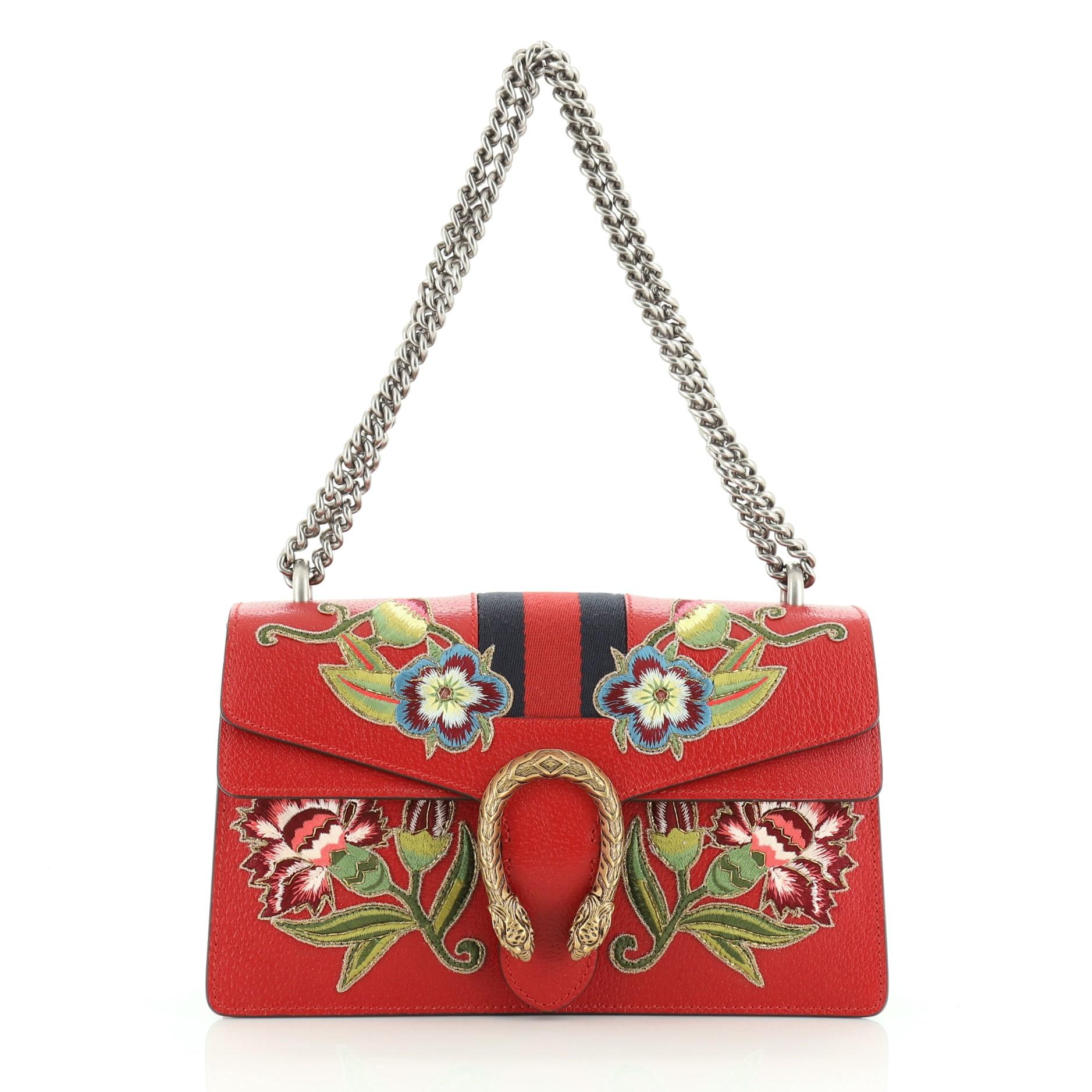 This Gucci Web Dionysus Bag Embroidered Leather Small, crafted from red leather, features chain link strap, textured tiger head spur detail on its flap, floral embroidery, and aged gold and aged silver-tone hardware. Its hidden push-pin closure
