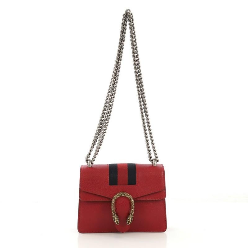 This Gucci Web Dionysus Bag Leather Mini, crafted from red leather, features a chain link strap, textured tiger head spur detail on its flap, web stripe detailing, and aged silver and gold-tone hardware. Its hidden push-pin closure opens to a beige