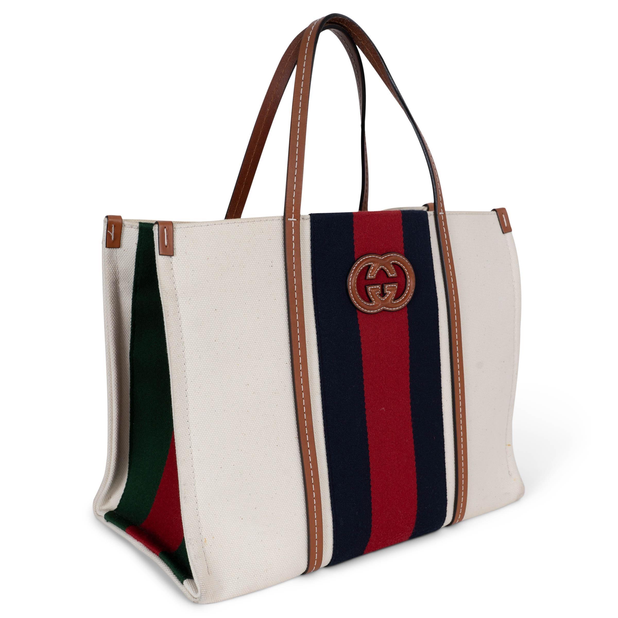 This 100% authentic Gucci Interlocking G Medium Tote is crafted from white canvas with the signature blue-red web stripe on the front and back and green-red web stripes on the gussets. Trimmed in cognac leather with contrast topstitching and a