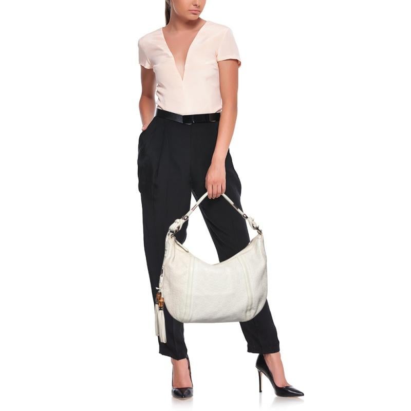This Gucci Horsebit hobo is perfect to carry on lunch outings and vacations! It has been designed using white leather and flaunts a gorgeous bamboo tassel detail on the side. It is finished with a single handle and a zip closure that opens into a
